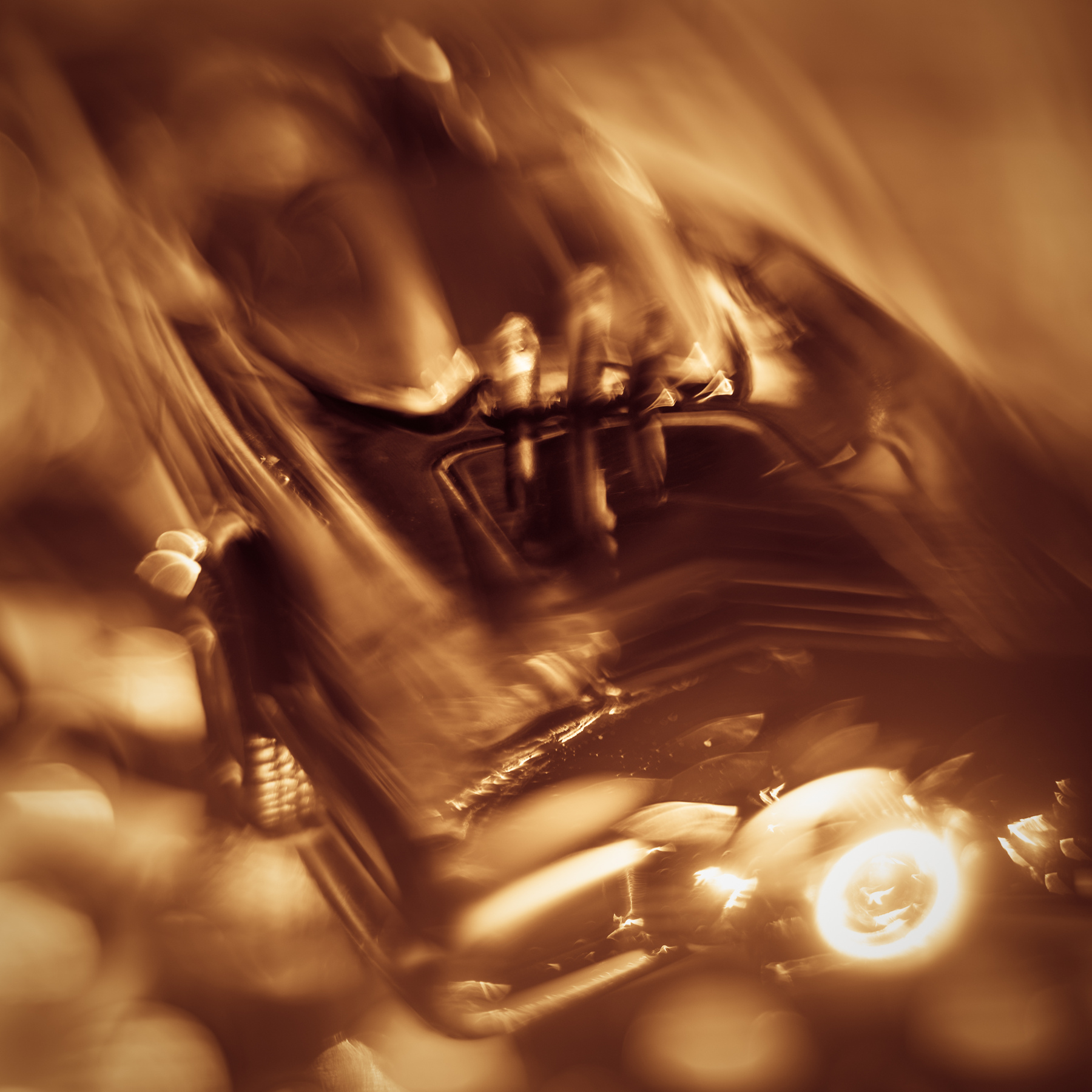 Close-up of a motorcycle with a blurred background, in warm tones, showing handlebars and headlight.