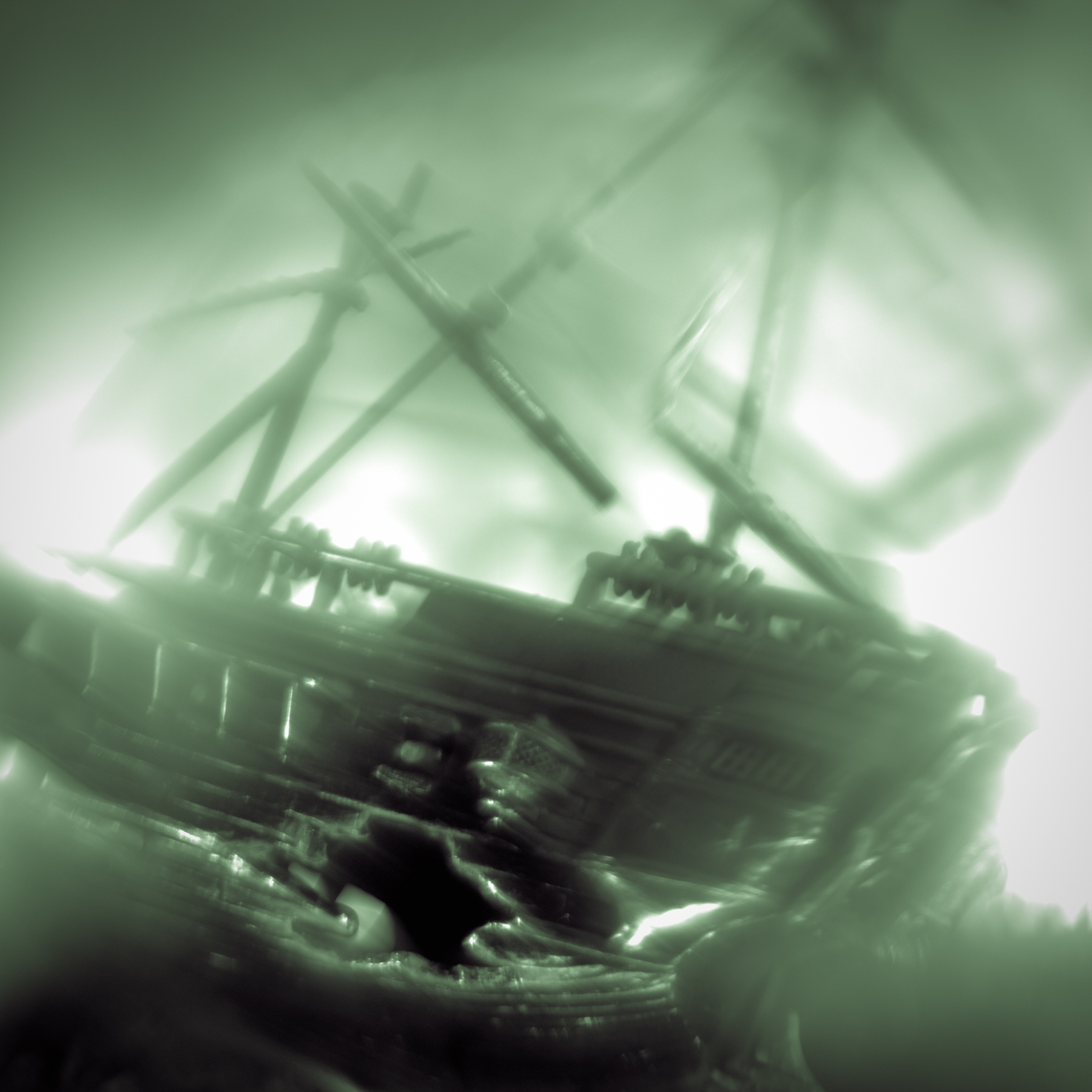 A ship with sails and masts is tilted, appearing to be sinking or damaged, with a person nearby in water.