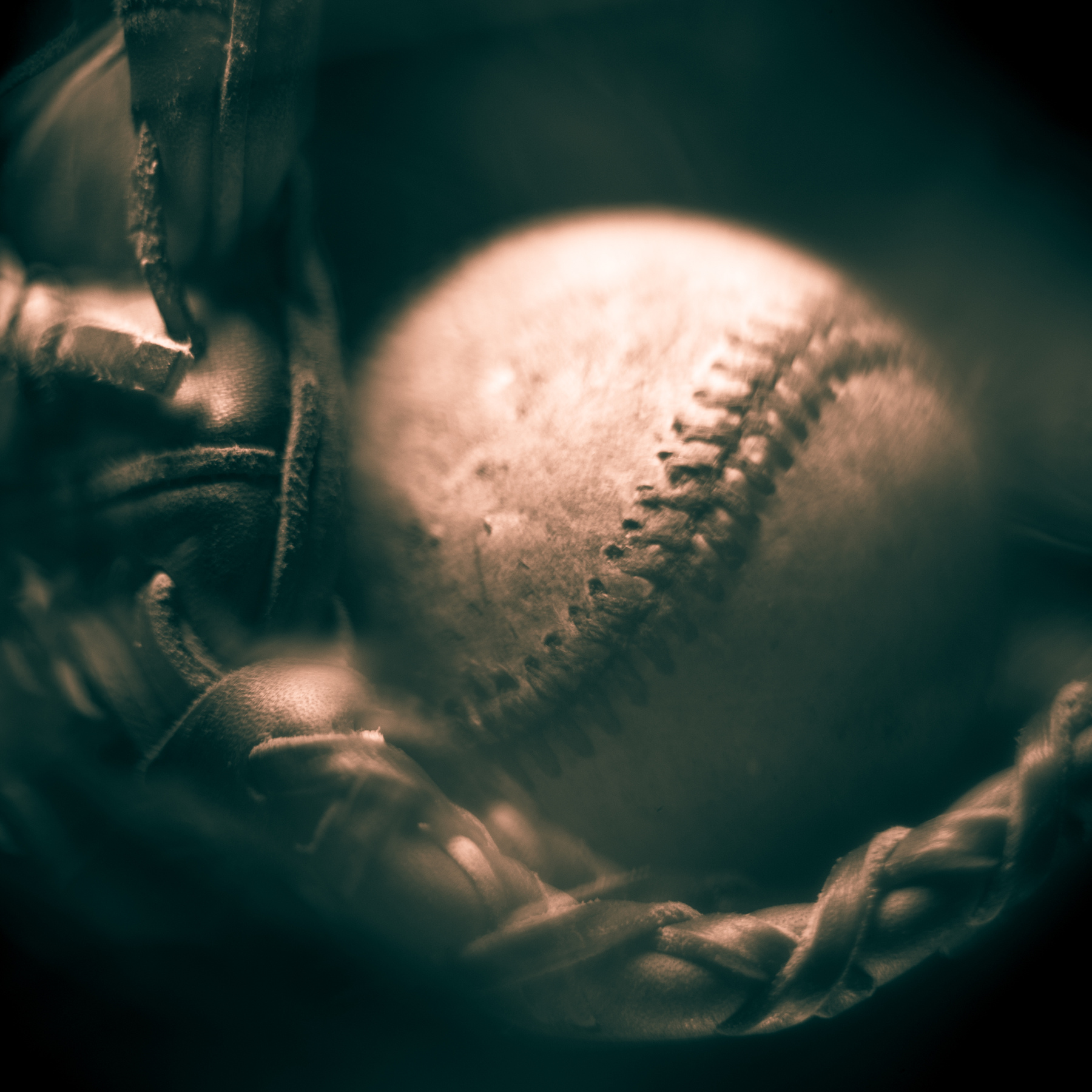 Close-up of a baseball inside a glove with a braided strap, in sepia tone.