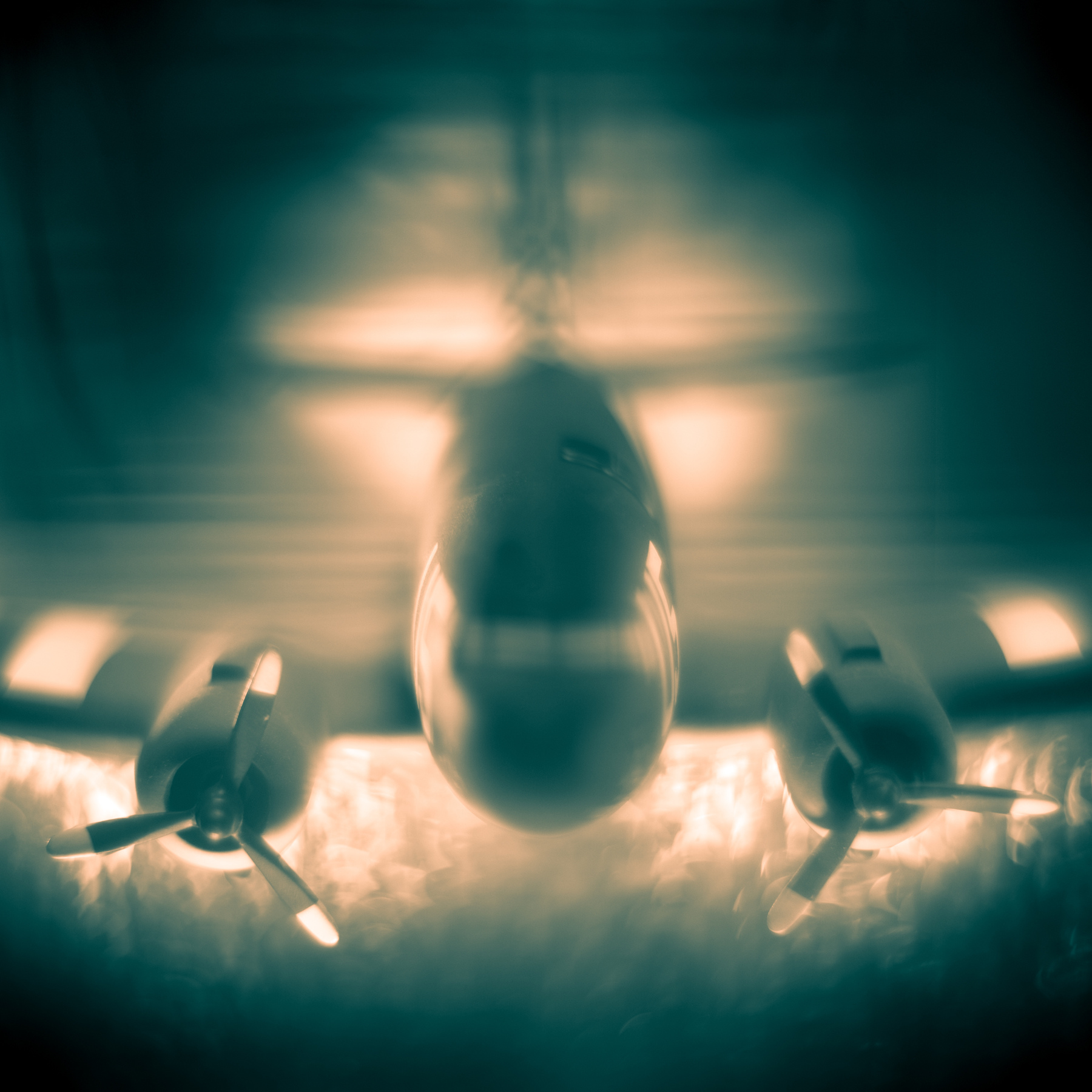 Aerial view of a military aircraft flying above clouds with engines visible, illuminated by sunlight, upside down in the image.