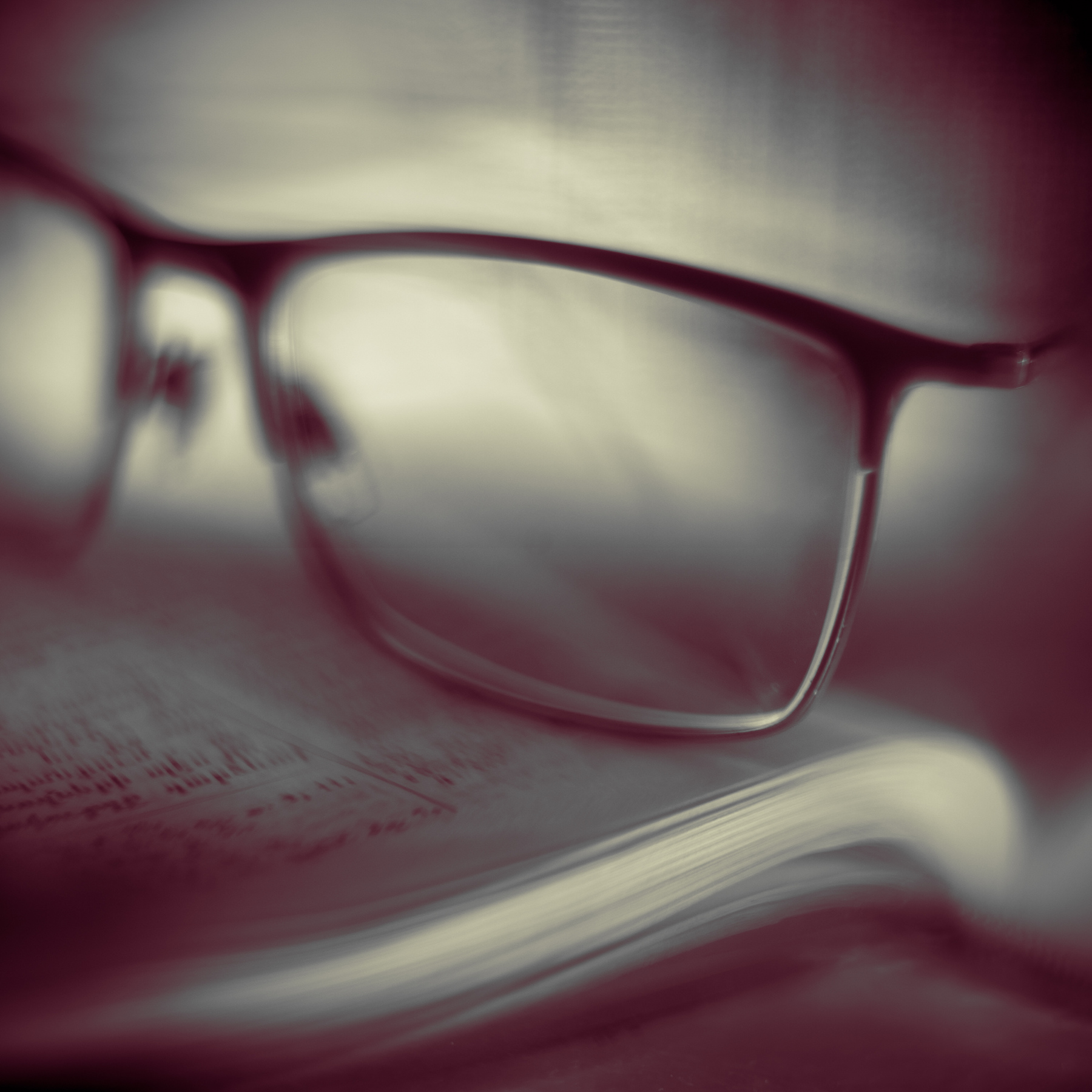 Close-up of eyeglasses resting on an open book, with a blurred background.