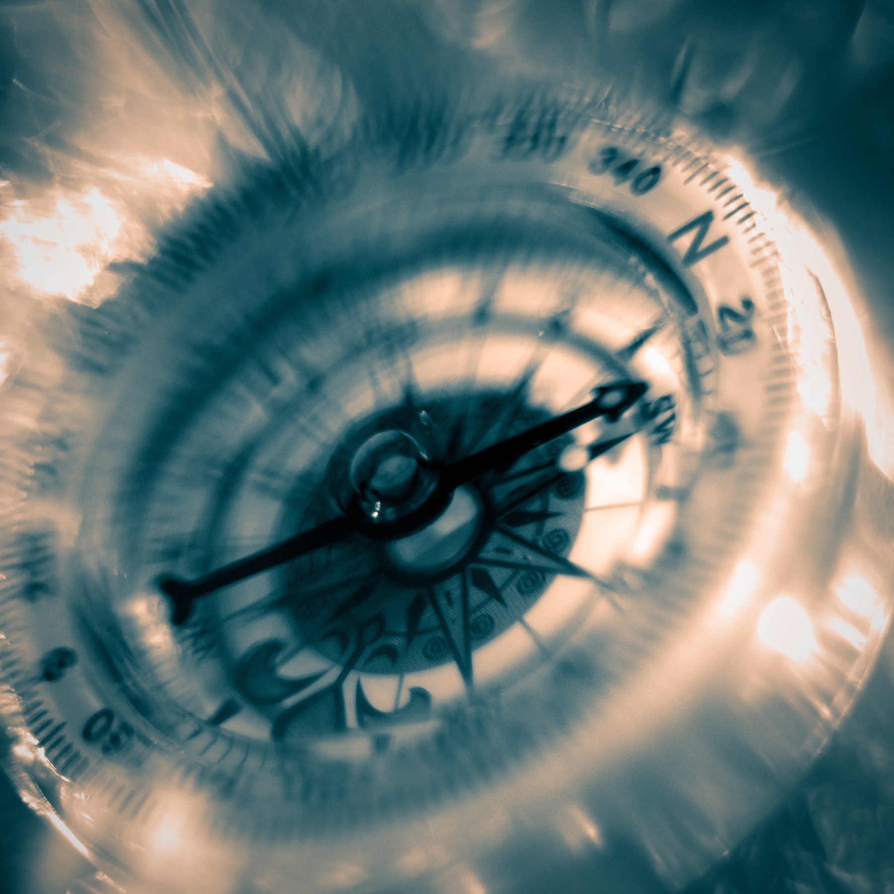 A compass with a blurred background, showing the needle pointing between 20 and 30 degrees, with a cloudy sky reflection.