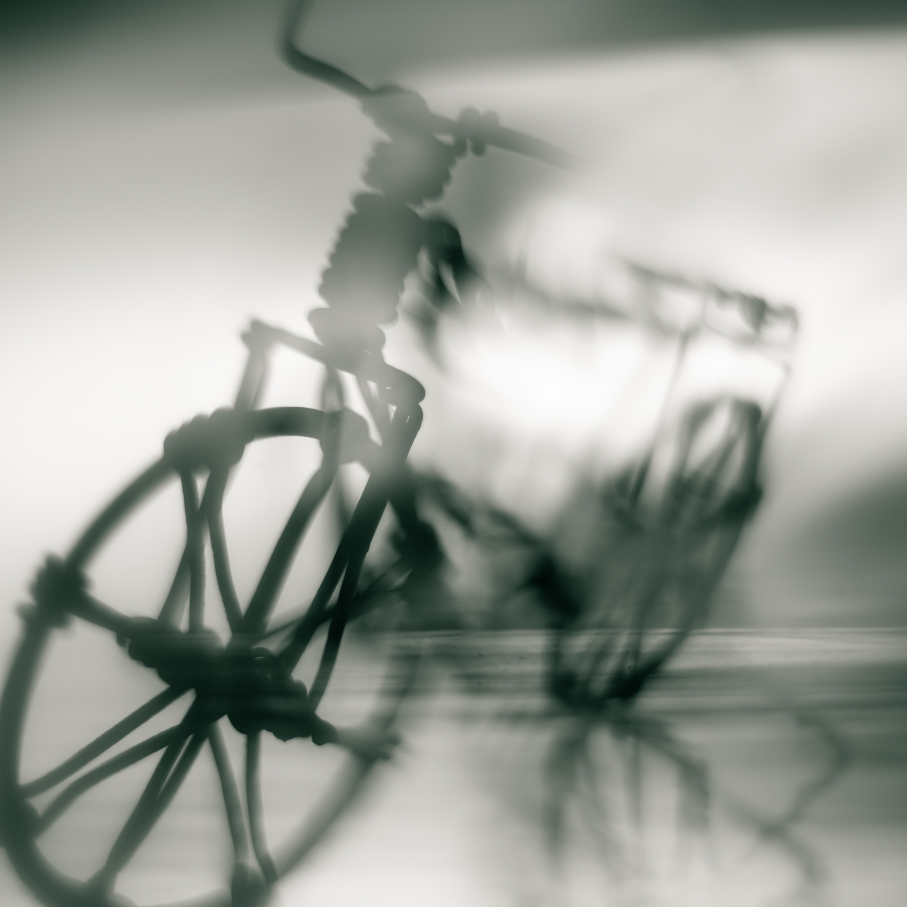 Blurred image of a bicycle with a wheel and handlebars visible, in black and white.