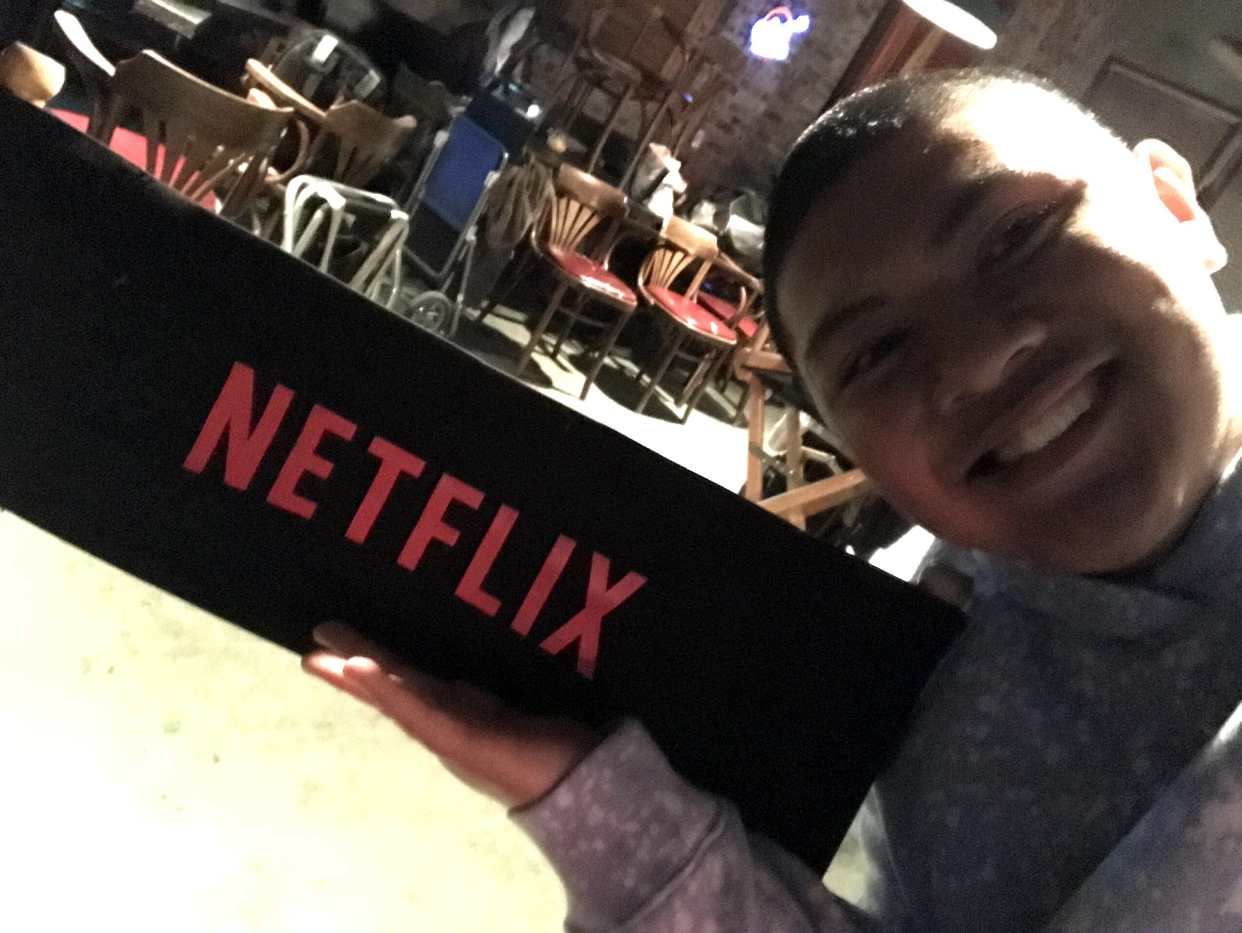 Person smiling holding a Netflix box in a restaurant or cafe setting.
