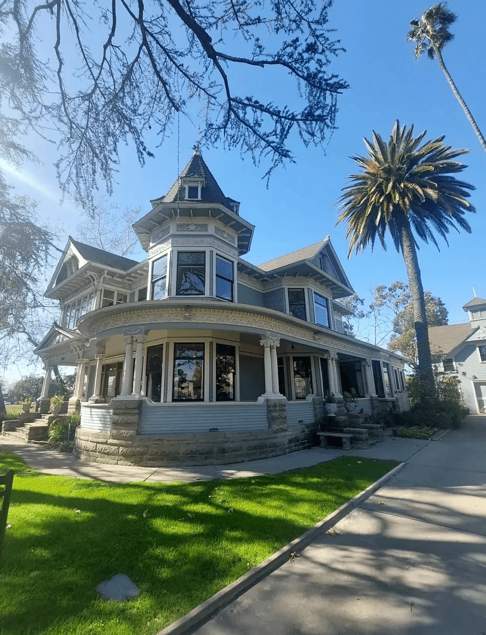 Victorian-style house with multiple turrets, large windows, and a wraparound porch, surrounded by trees and a grassy lawn.