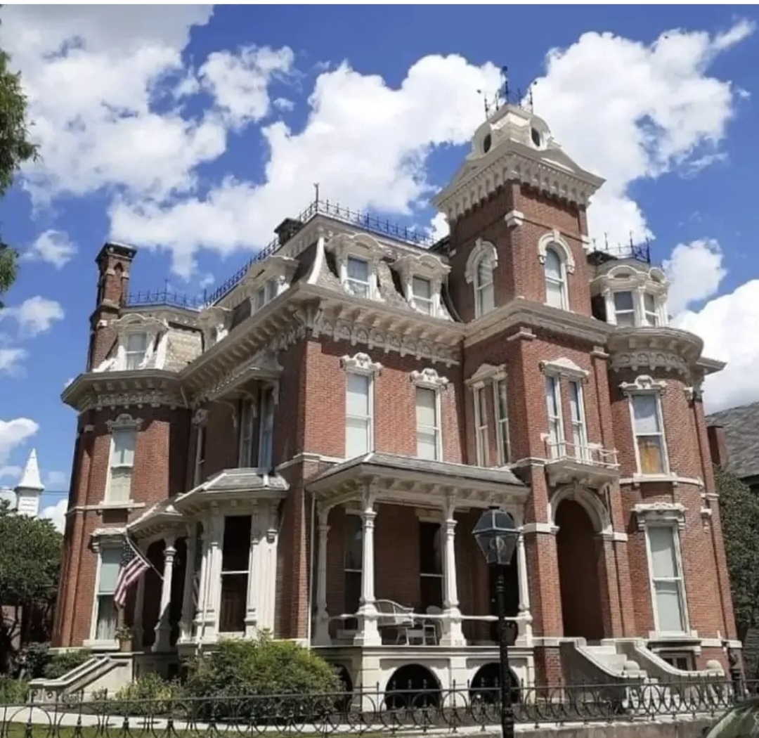 Victorian-style brick mansion with towers, balconies, and decorative trim under a partly cloudy sky.