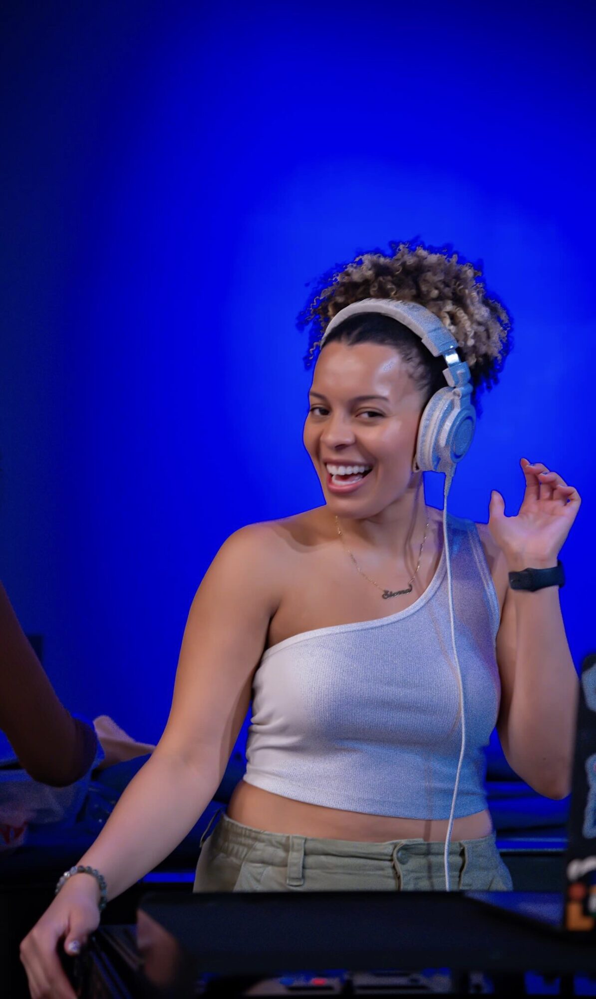 Woman with curly hair wearing headphones, smiling, in front of a blue background.