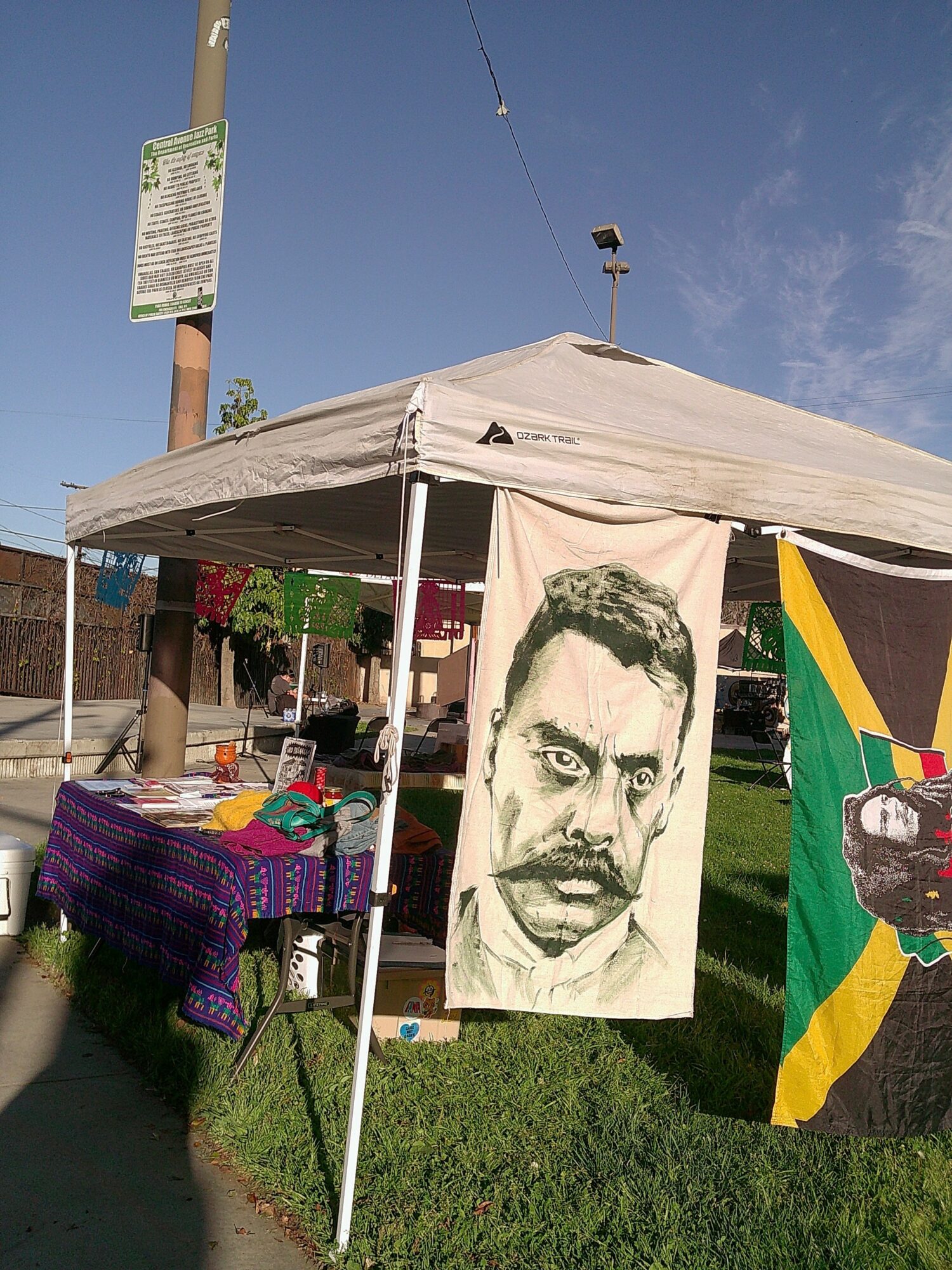 Street vendor stall with a large black-and-white portrait of a man hanging, and a Jamaican flag beside it, under a canopy.