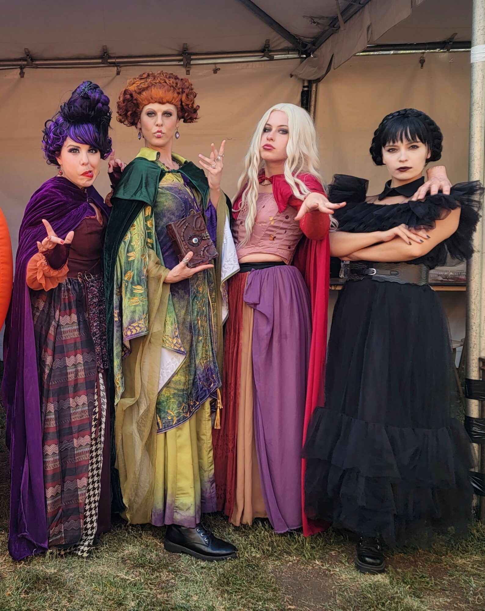 Four women in colorful costumes standing together inside a tent, posing for a photo.