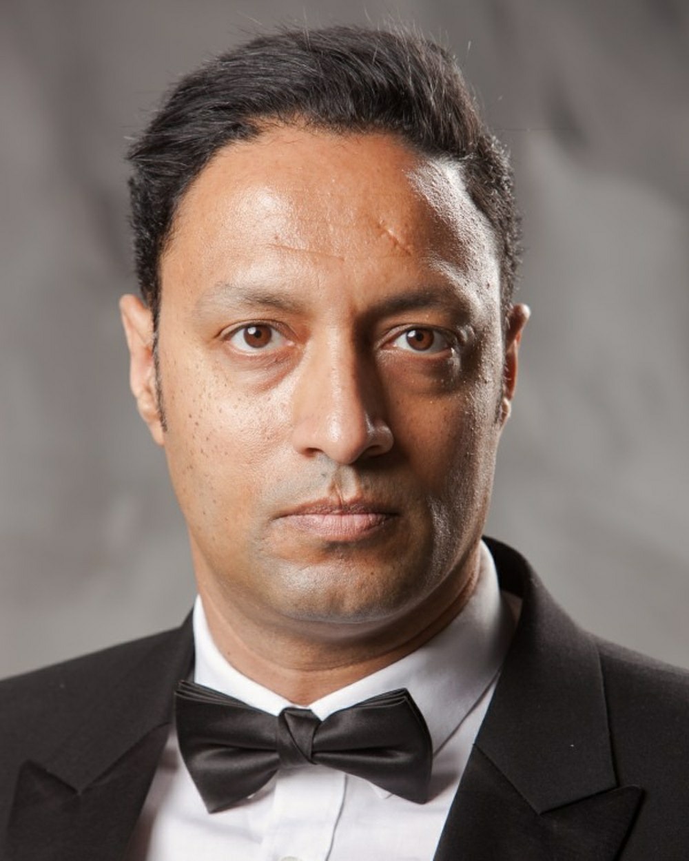 Portrait of a man in a tuxedo with a bow tie, looking directly at the camera, neutral expression.