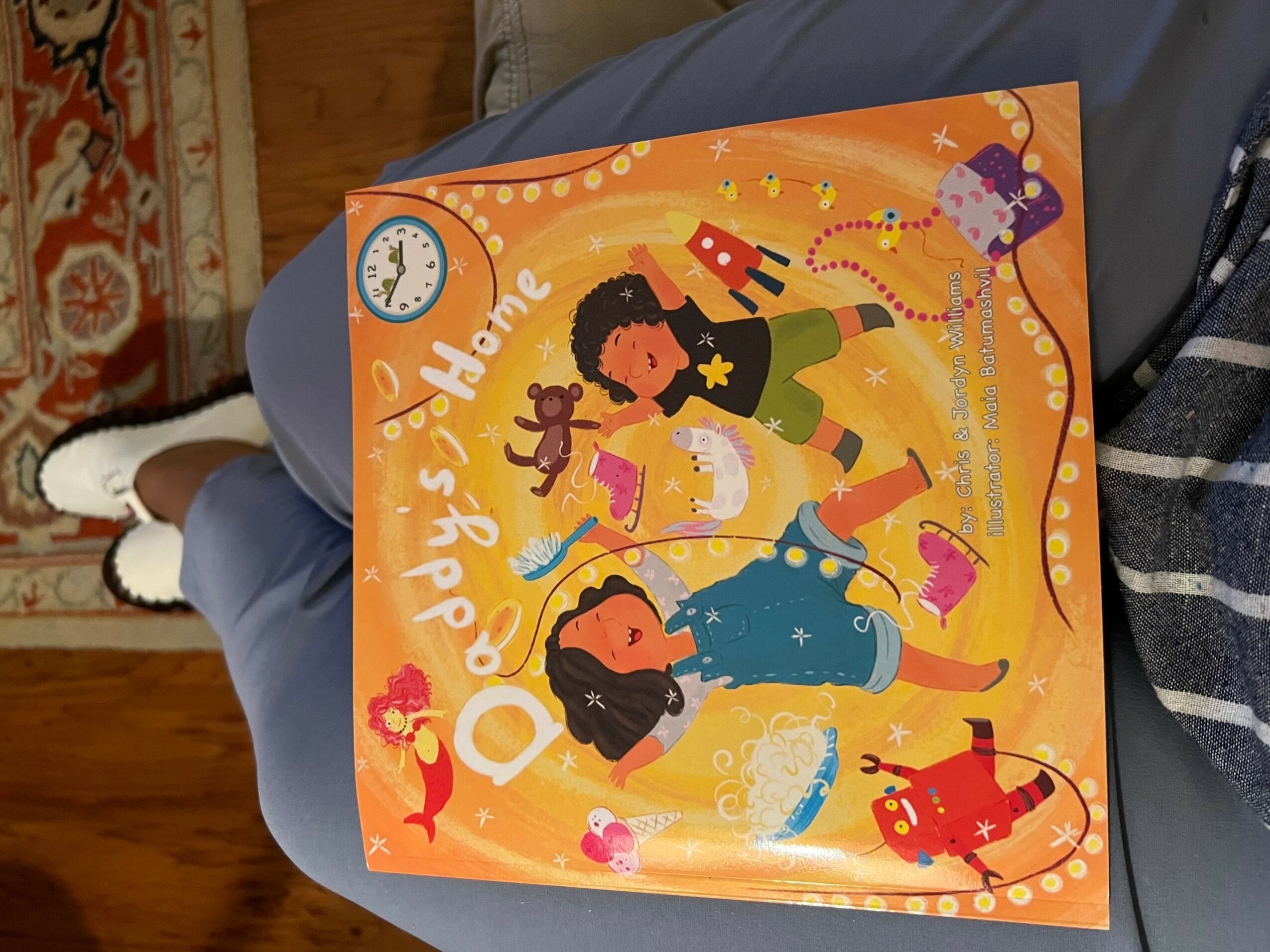 Colorful children's book cover with two girls, a cat, and a dog, surrounded by stars and hearts, titled 'O Happy's Home'.