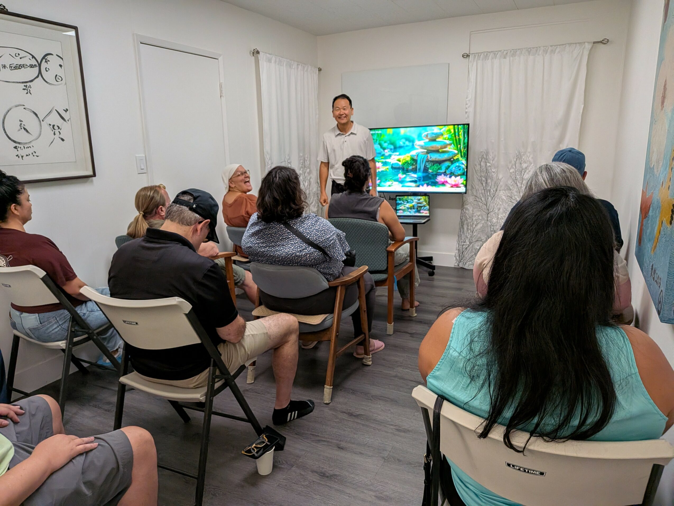 Group of people seated in a room listening to a person presenting in front of a colorful aquarium display on a screen.