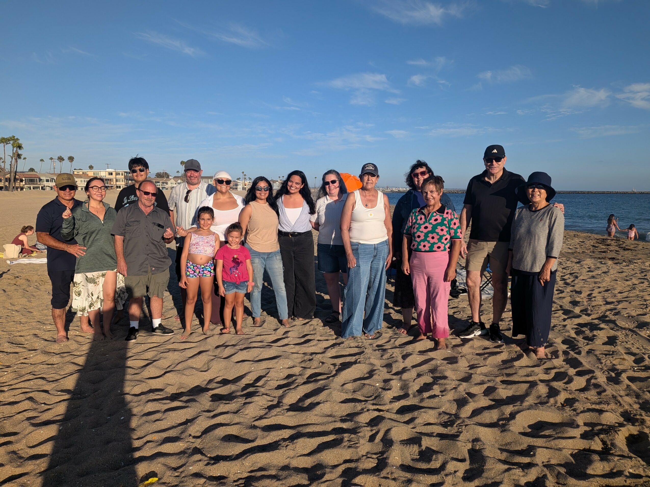 Group of people standing on a sandy beach with the ocean and blue sky in the background.