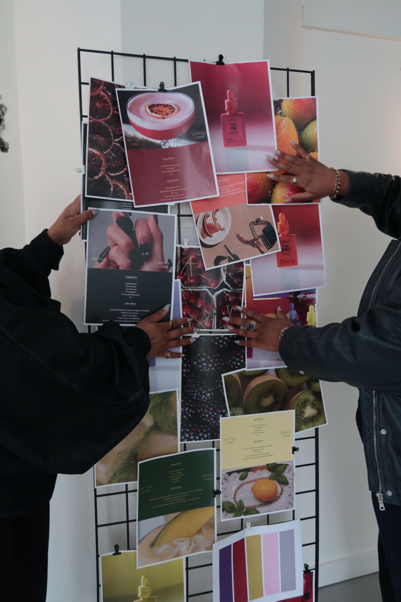 Two people hold a display board with various colorful photographs and images, including food and abstract designs.