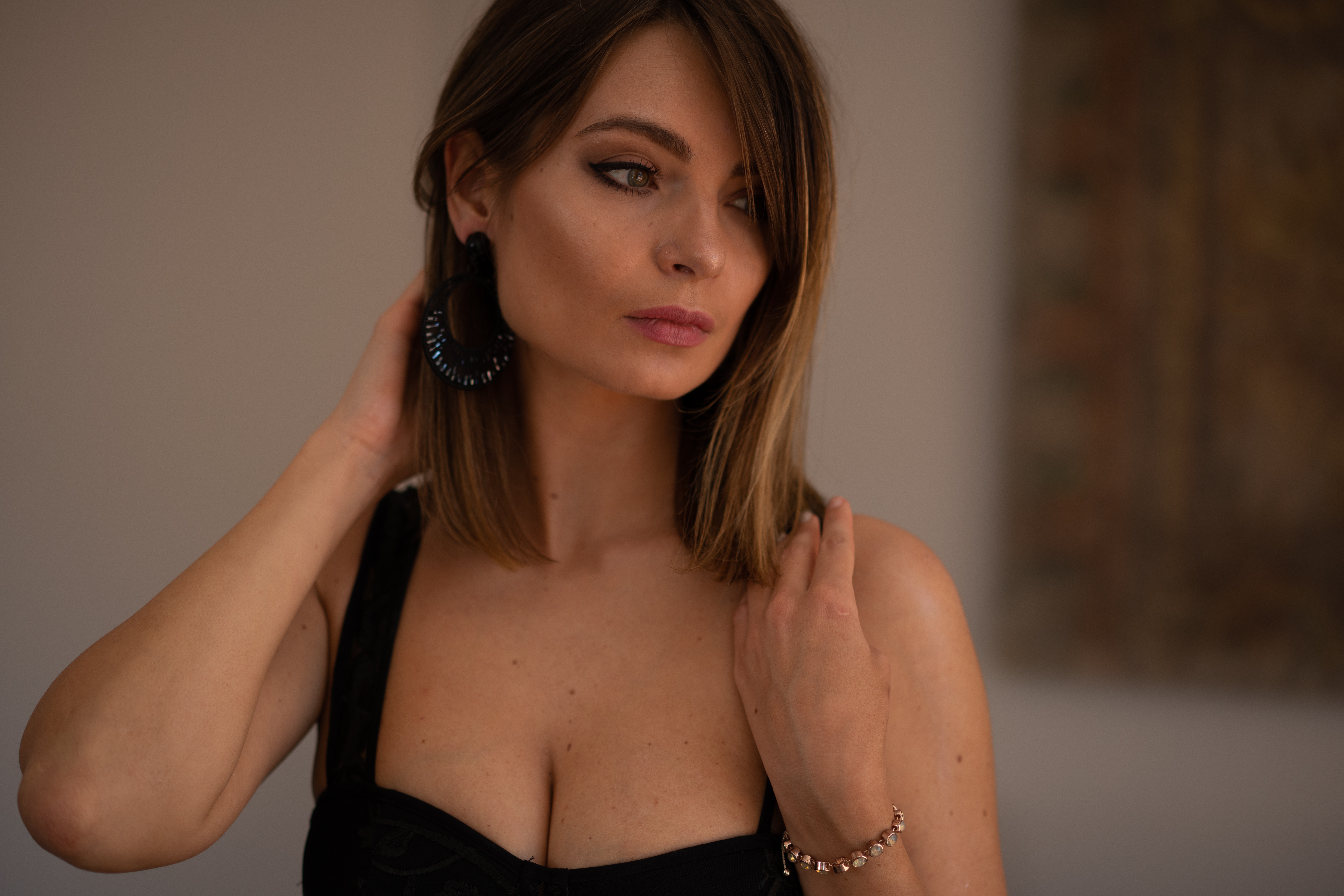 Woman with shoulder-length hair, wearing a black top, looking to the side, touching her neck and shoulder, indoors.