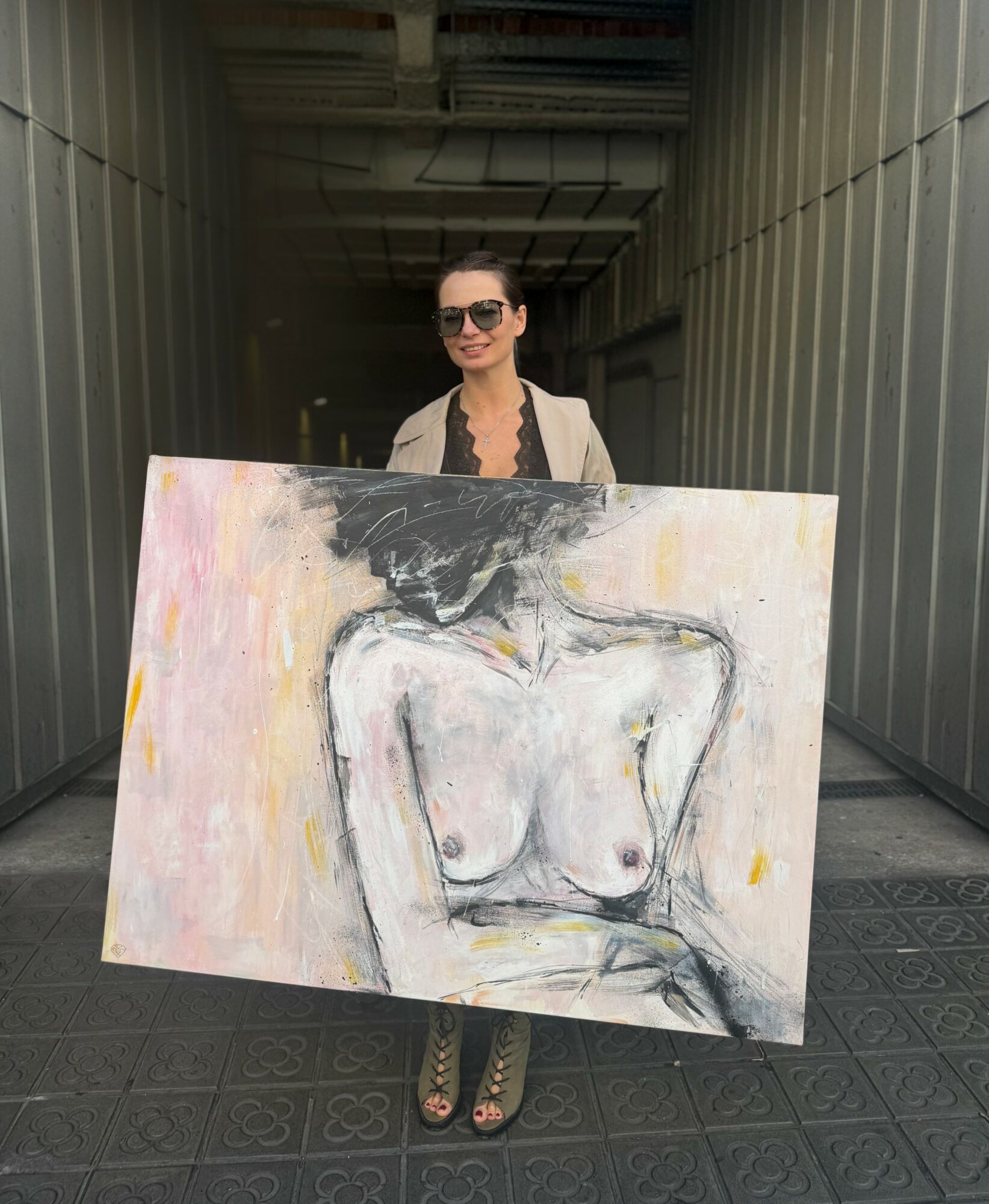 Person holding a large painting of a nude female figure, standing in a corridor with metal walls.