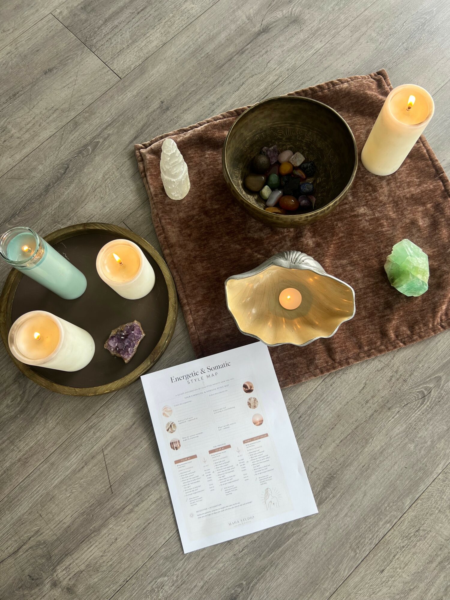 Arrangement of candles, crystals, and a sheet on a wooden floor with a brown cloth, creating a calming scene.