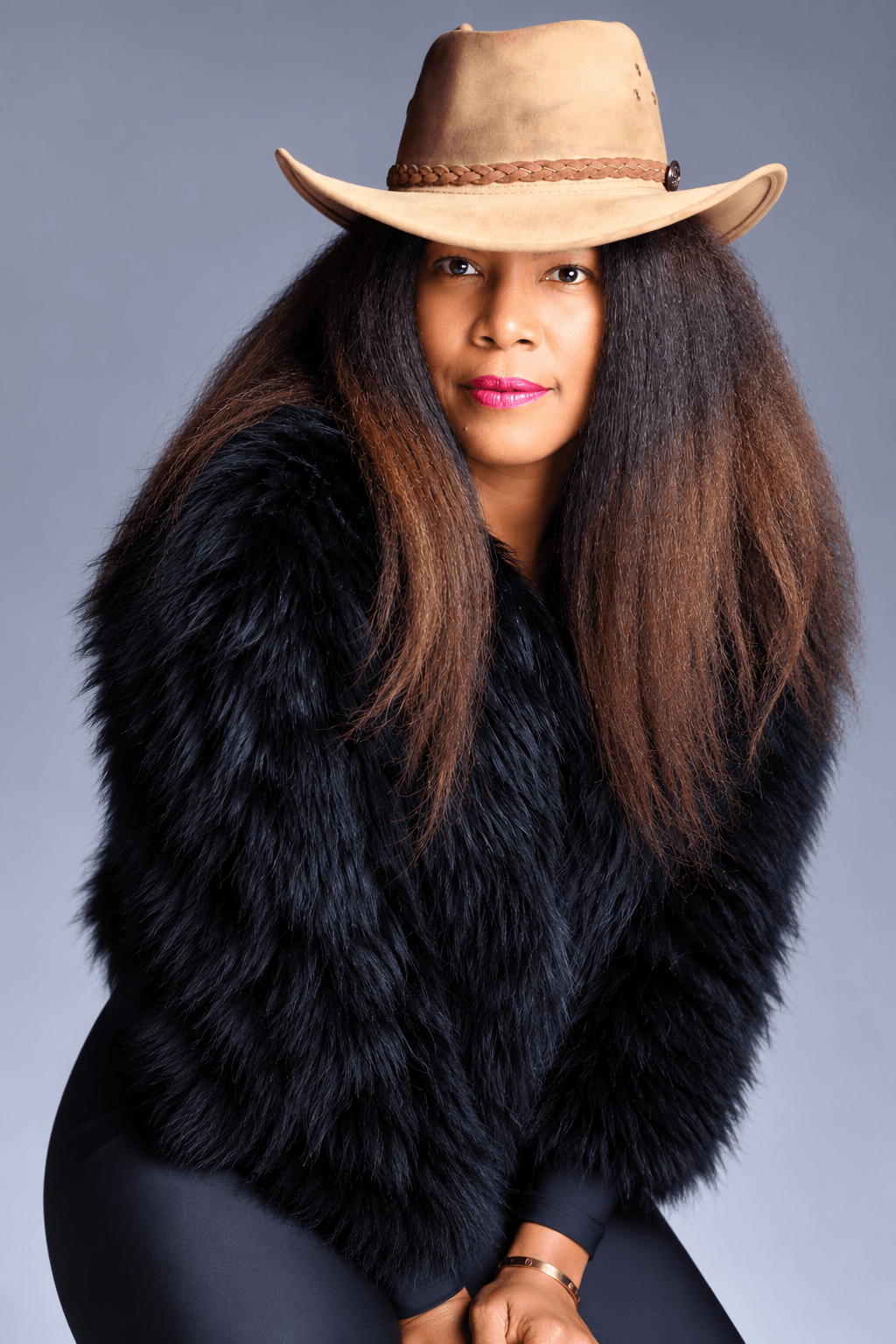 Woman with long hair wearing a wide-brimmed hat and black fur coat, looking at the camera.