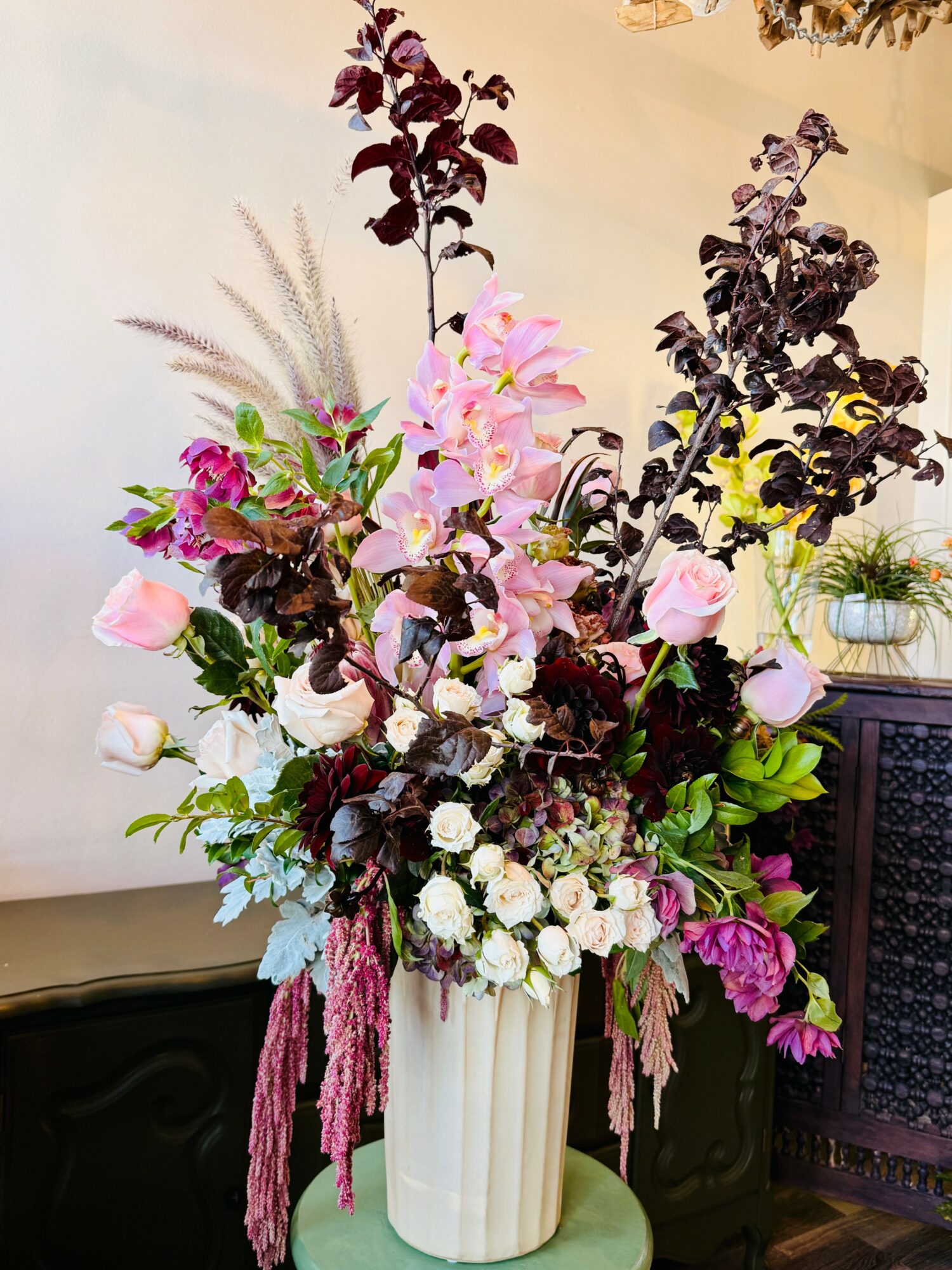 Large floral arrangement with pink, white, and dark purple flowers in a white vase, on a green surface.