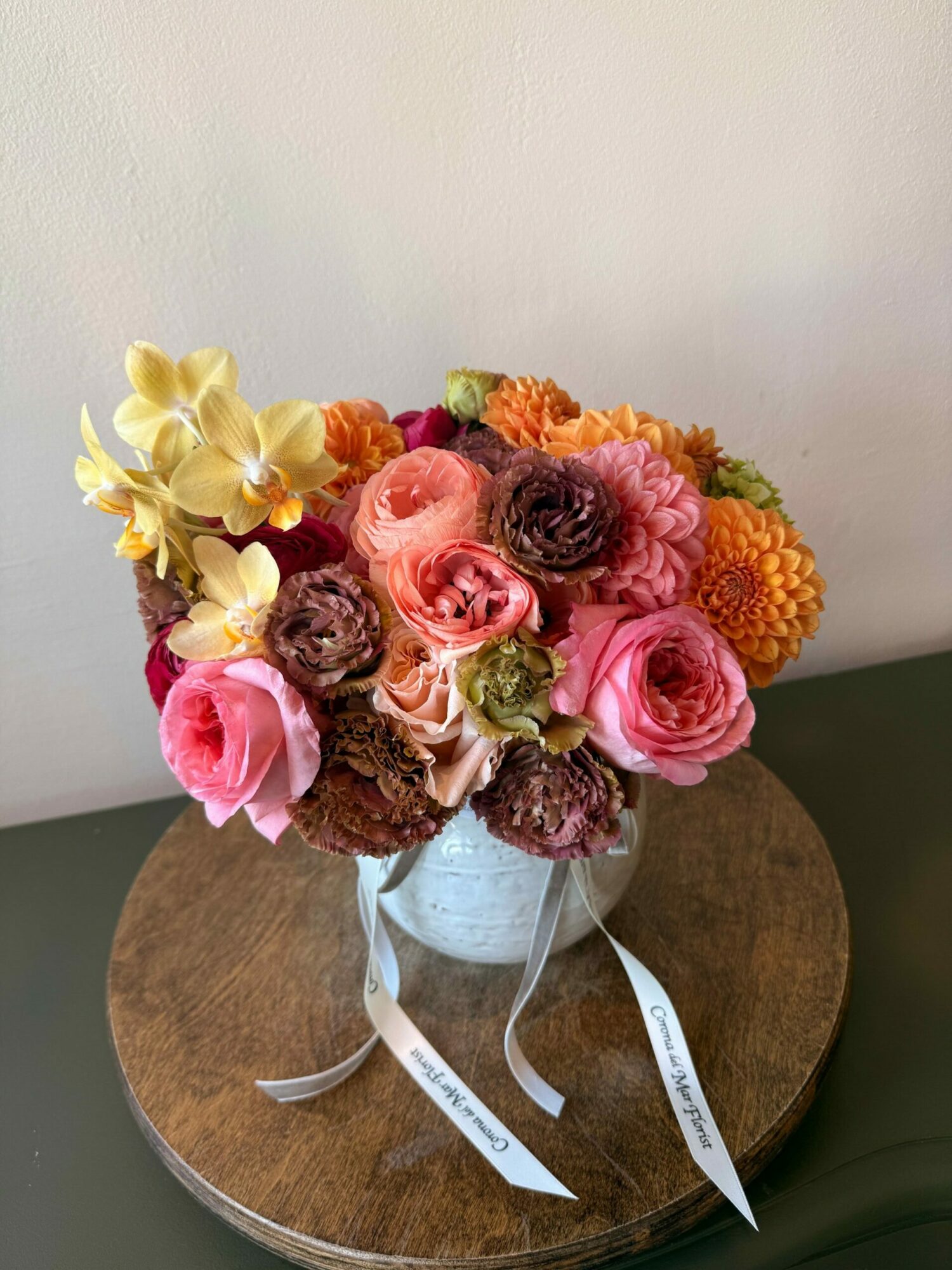 Bouquet of pink, orange, and yellow flowers on a round wooden table, with ribbons attached.