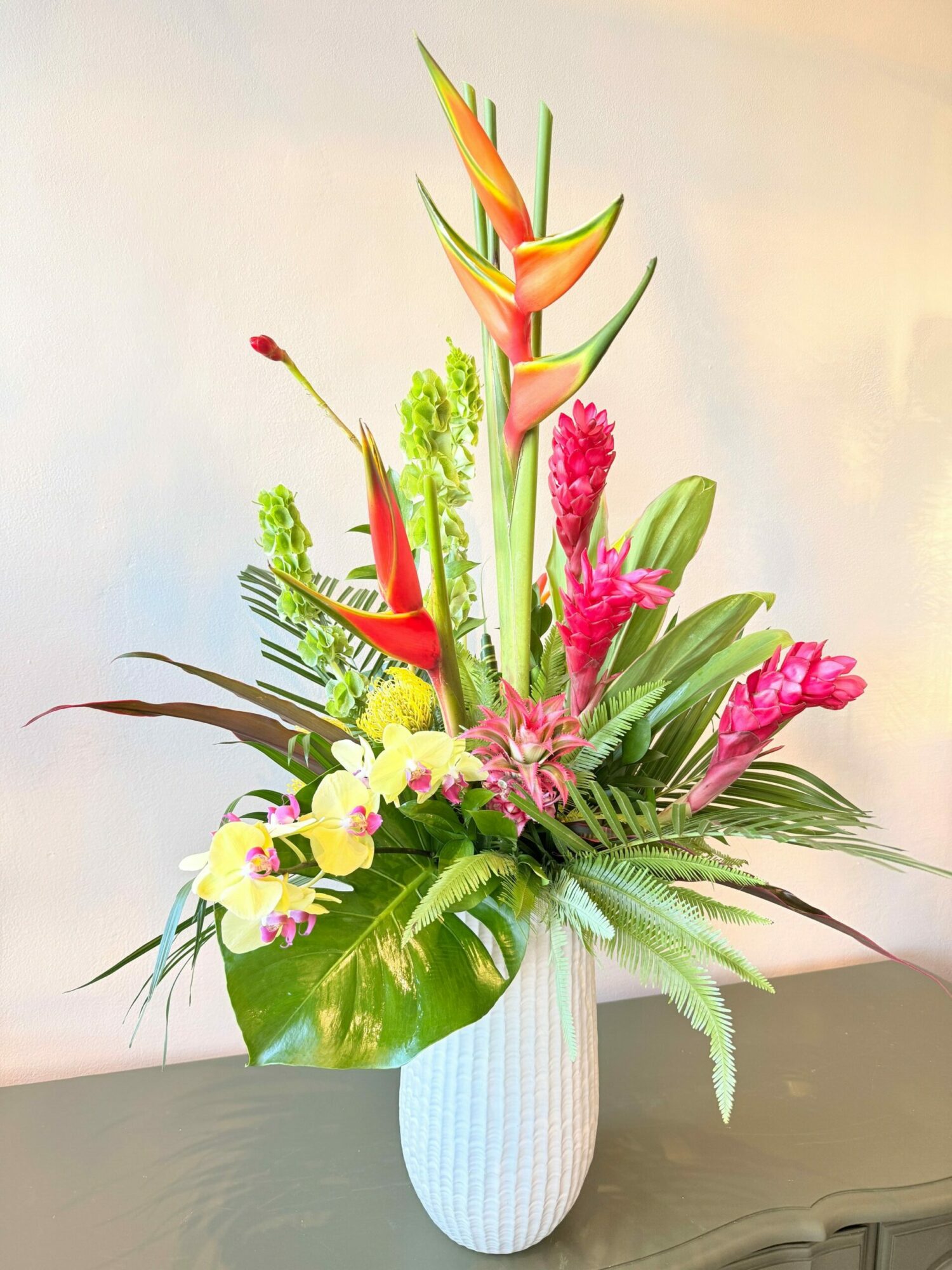 Colorful flower arrangement with pink, yellow, and orange flowers and green leaves on a white surface.