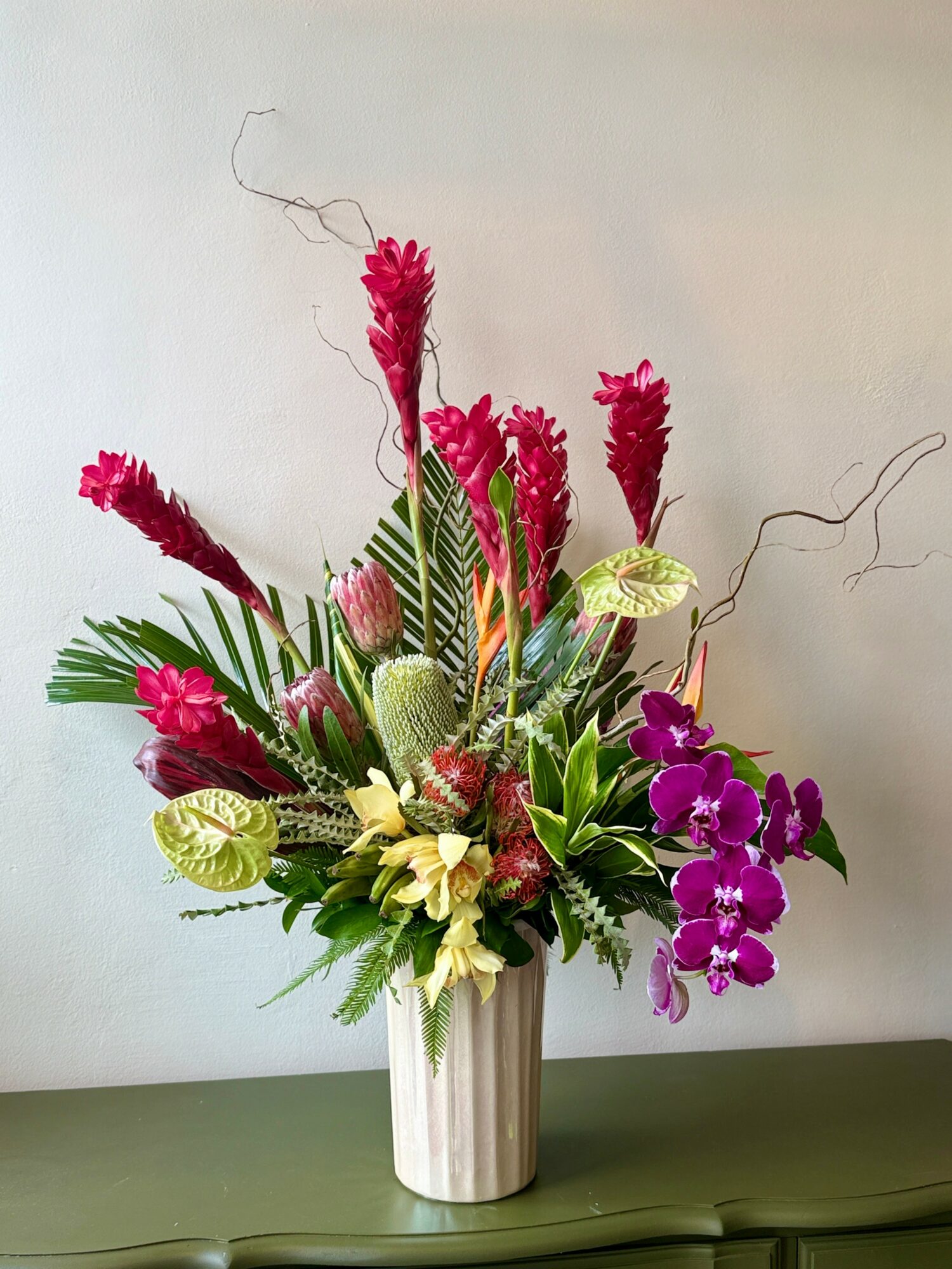 Colorful flower arrangement in a white striped vase with pink, purple, and yellow flowers, and green foliage.