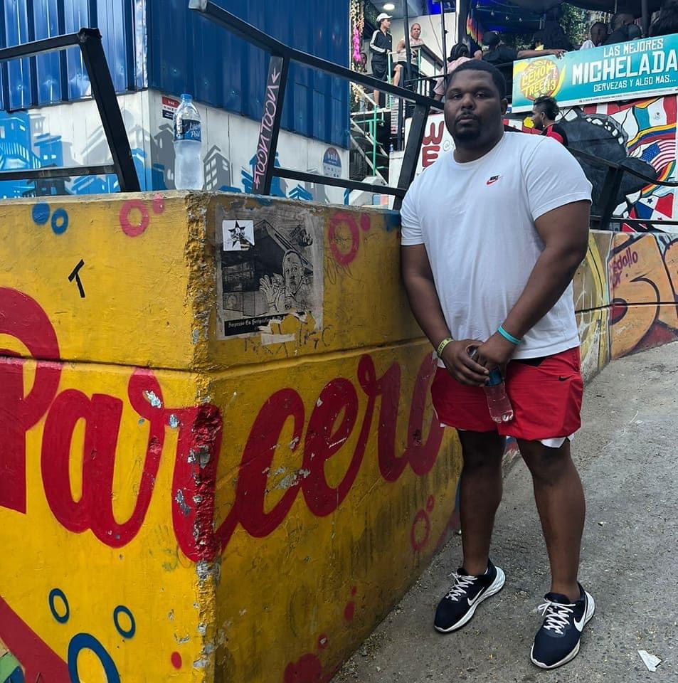 Man standing next to a colorful painted wall with text, wearing a white t-shirt, red shorts, and black sneakers.