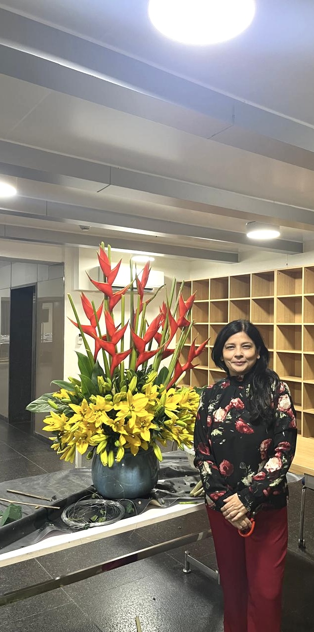 Woman standing next to a large flower arrangement with red and yellow flowers in a room with shelves.