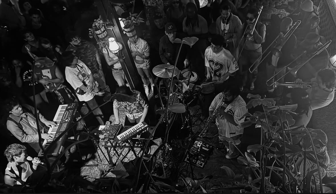 Group of people gathered around musical instruments and equipment in a dimly lit space.