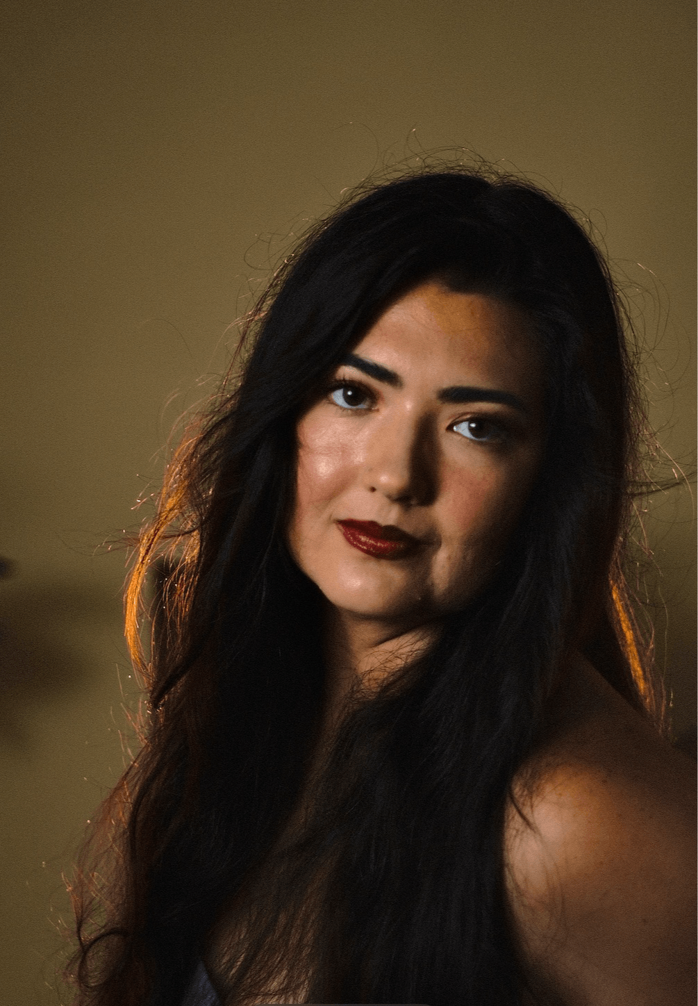 Portrait of a woman with long dark hair, dark lipstick, and a neutral background.