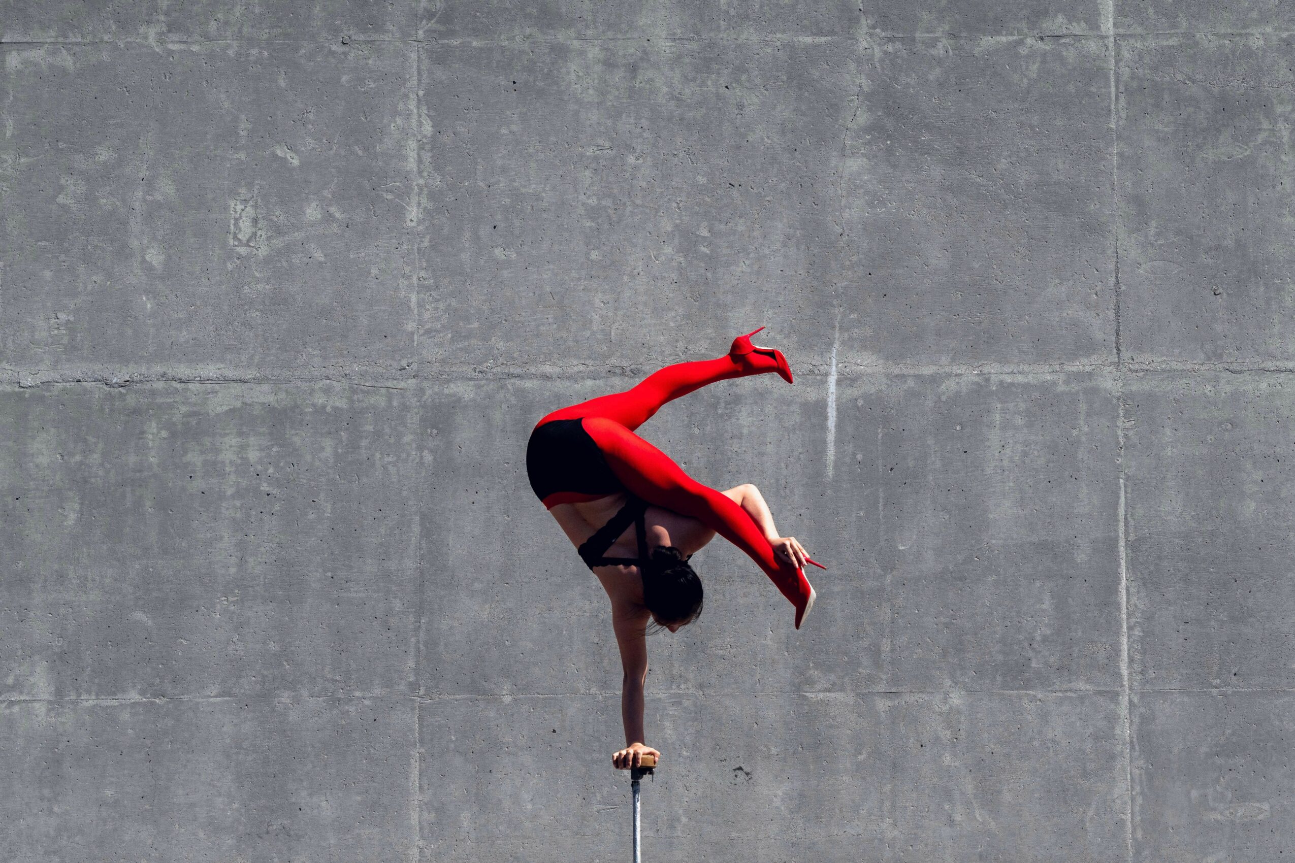 A person in red and black athletic clothing performs a handstand on a concrete surface.