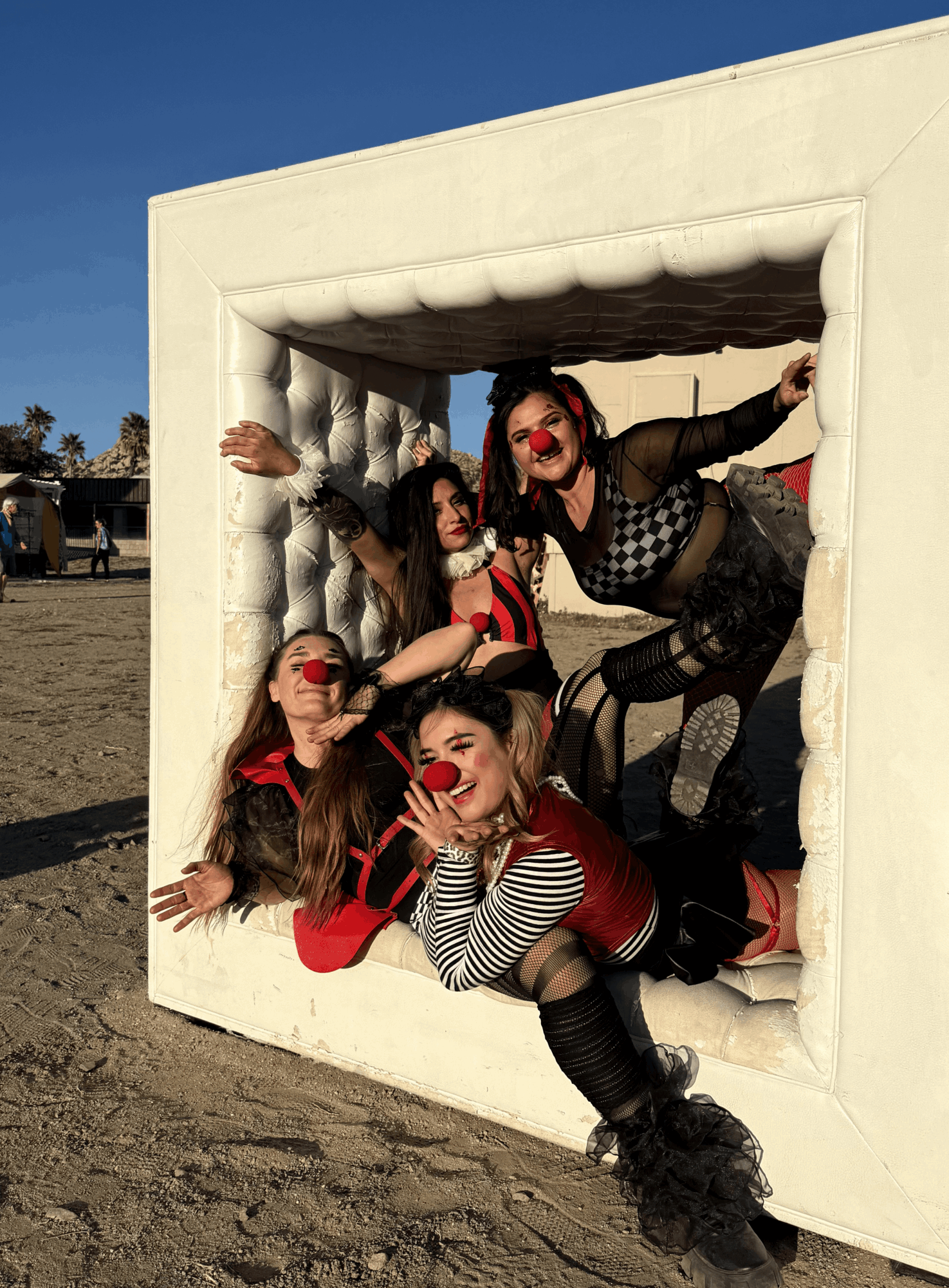 Four people with red noses and costumes pose inside a large white inflatable frame outdoors, smiling and making playful gestures.
