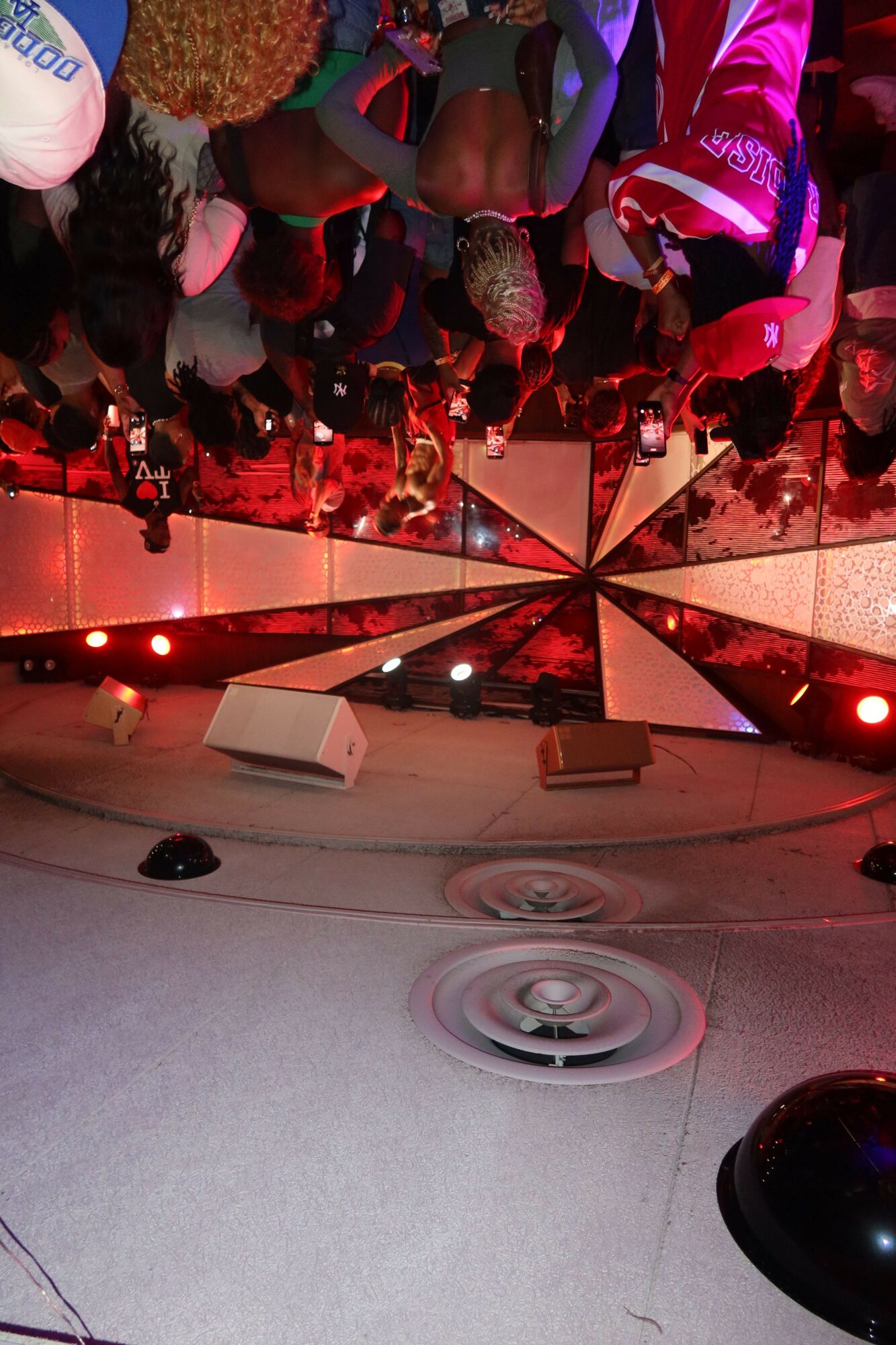 Crowd of people at a party or event, with colorful lighting and decorations, some wearing costumes or themed clothing.