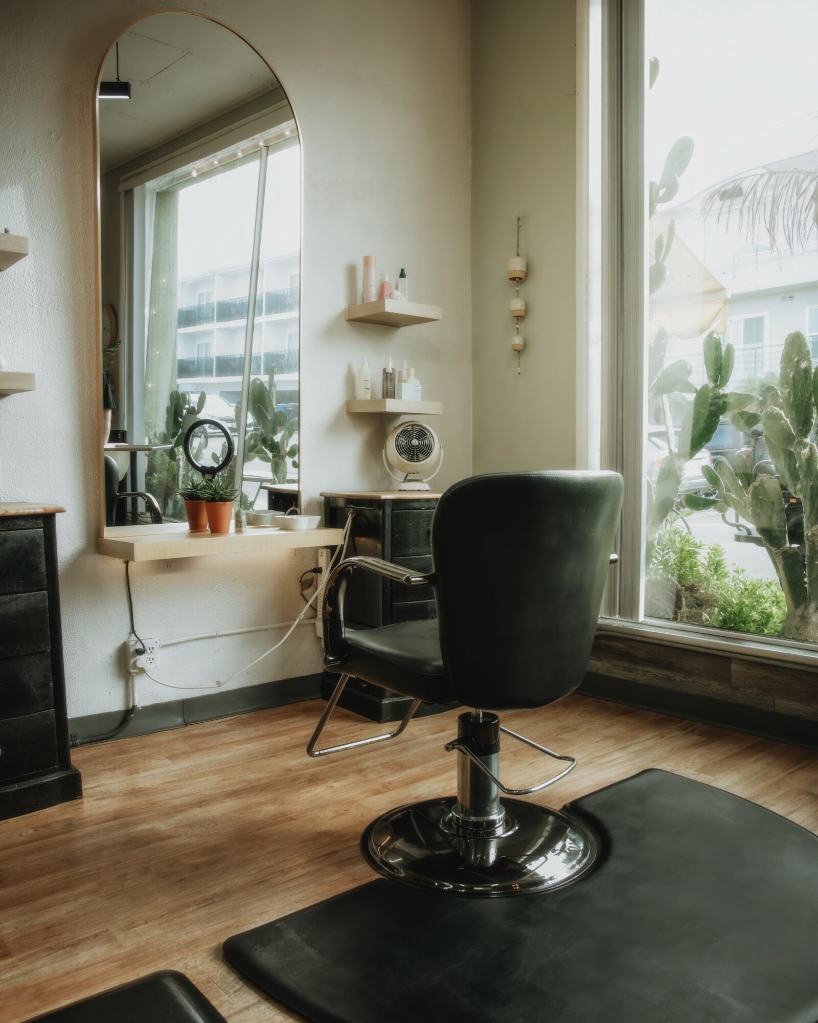 Interior of a room with a black chair, a large window, and shelves with decorative items, plants outside visible.