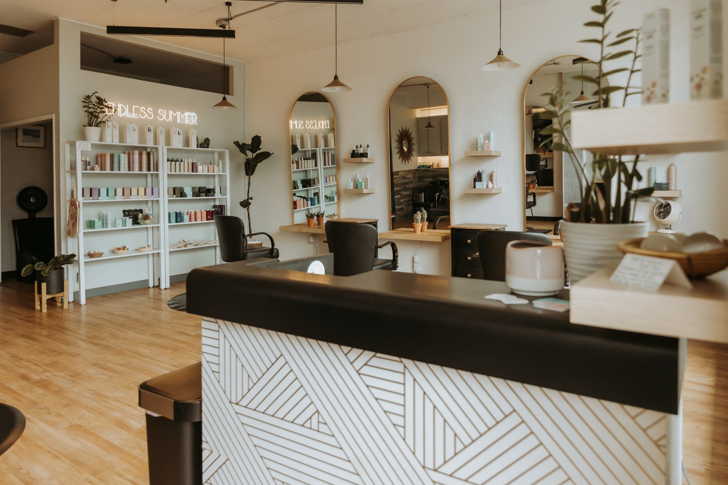 Interior of a bookstore or cafe with shelves, tables, chairs, and plants, featuring a wooden floor and arched mirrors.