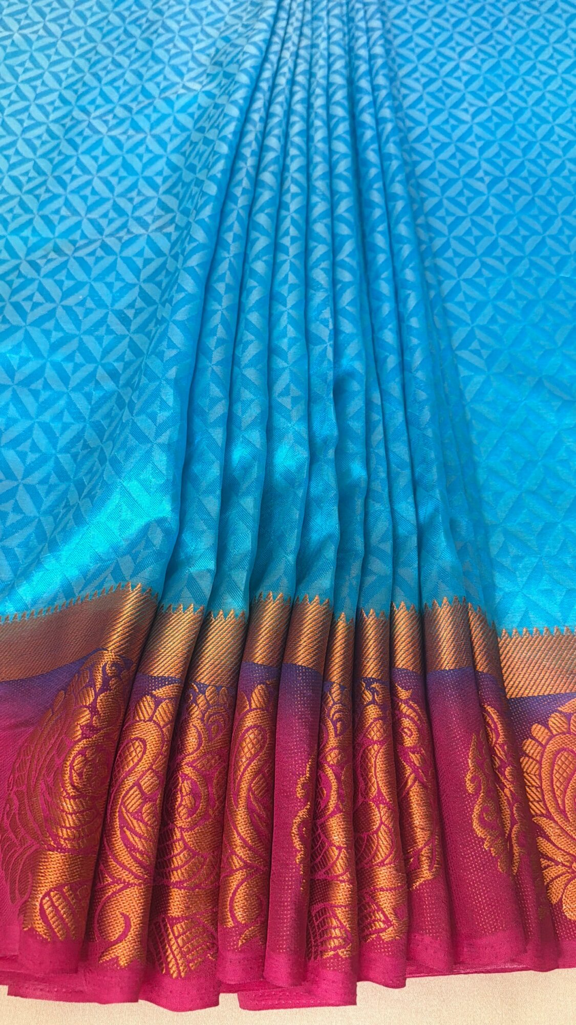 Bright blue fabric with a gold and pink border featuring floral patterns, pleated and draped.