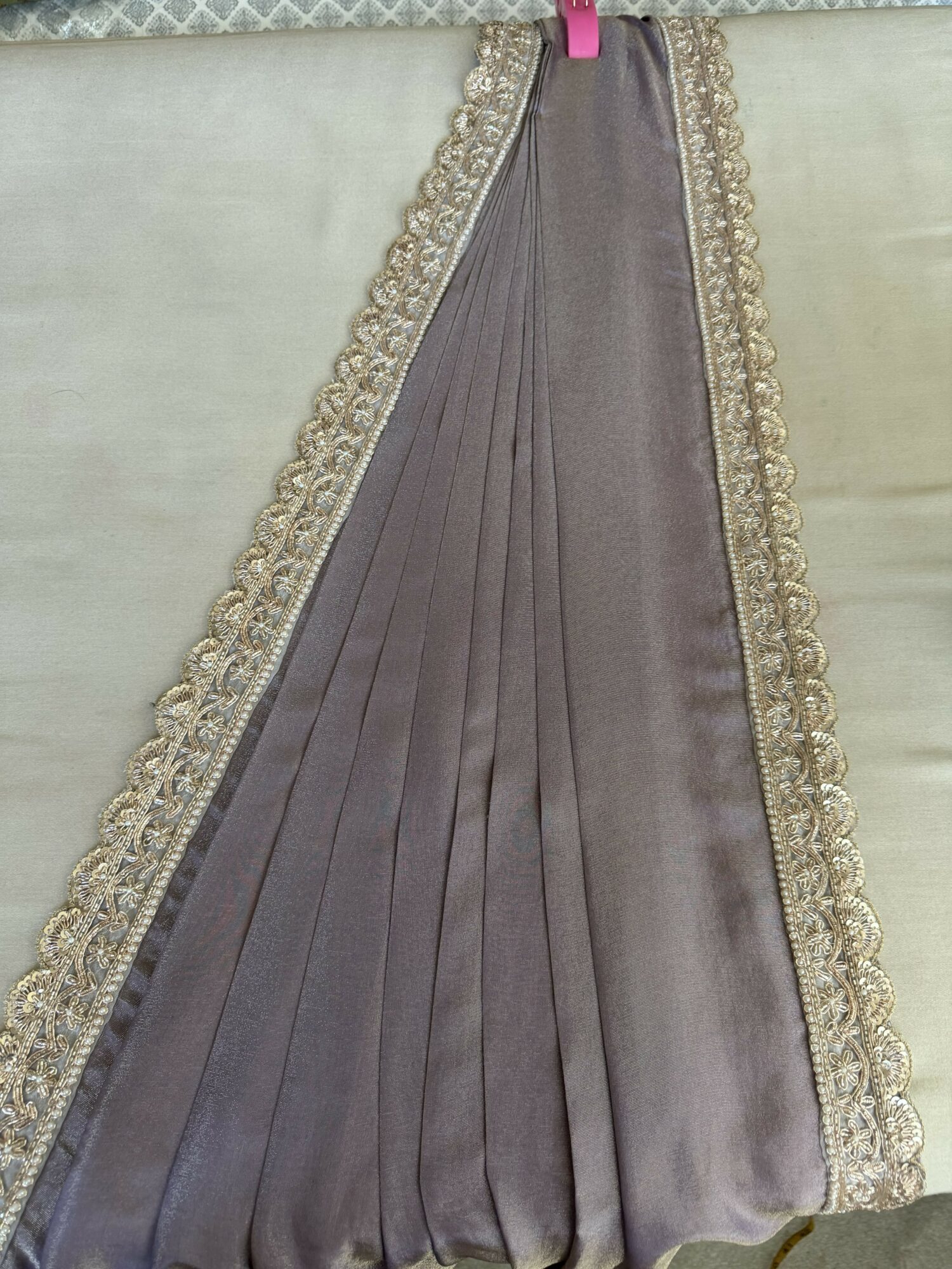 A pleated fabric with decorative trim along the edges, hanging vertically. The fabric appears to be satin or similar material.