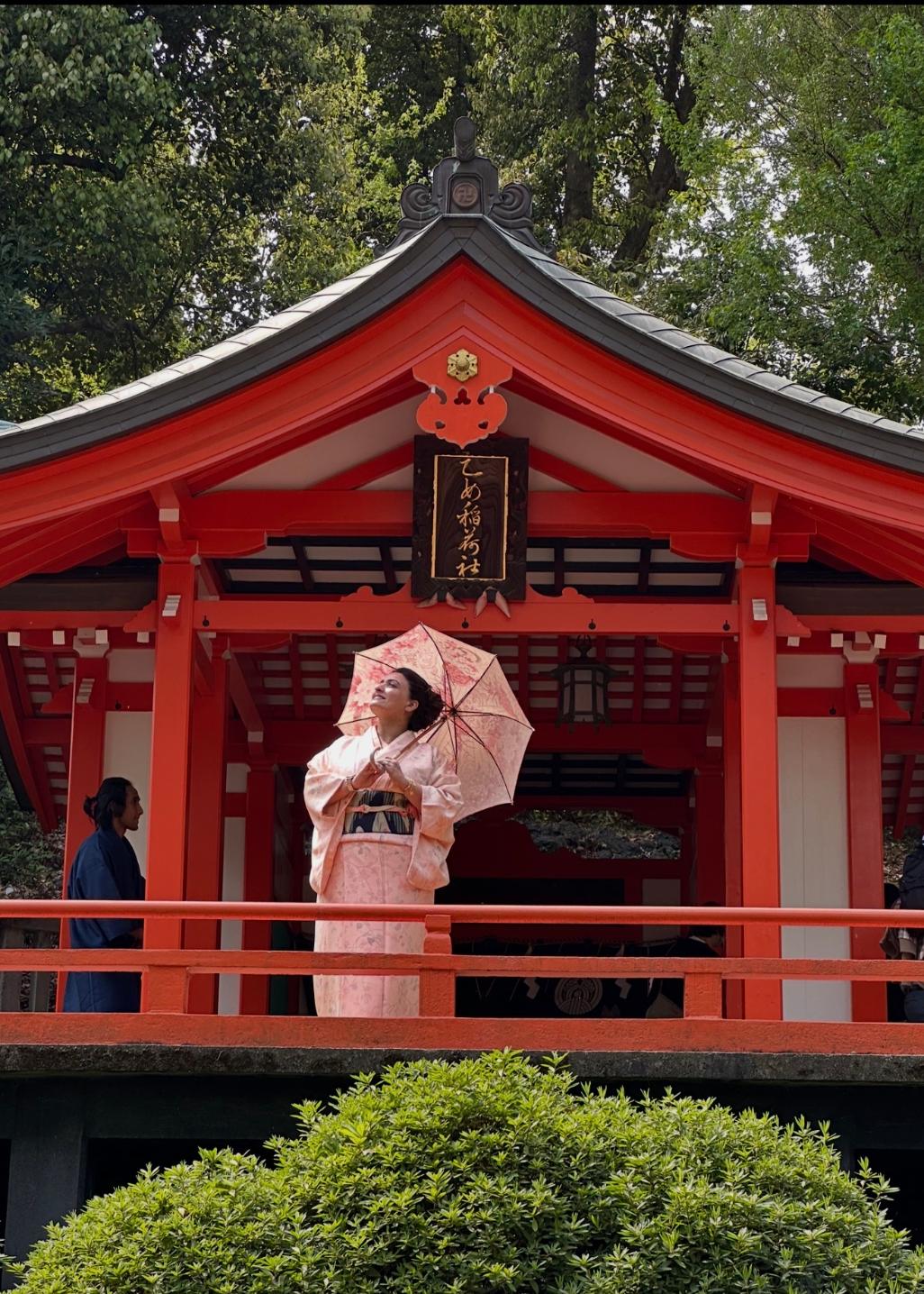Woman in traditional kimono holding a parasol on a red shrine balcony, with trees in background.