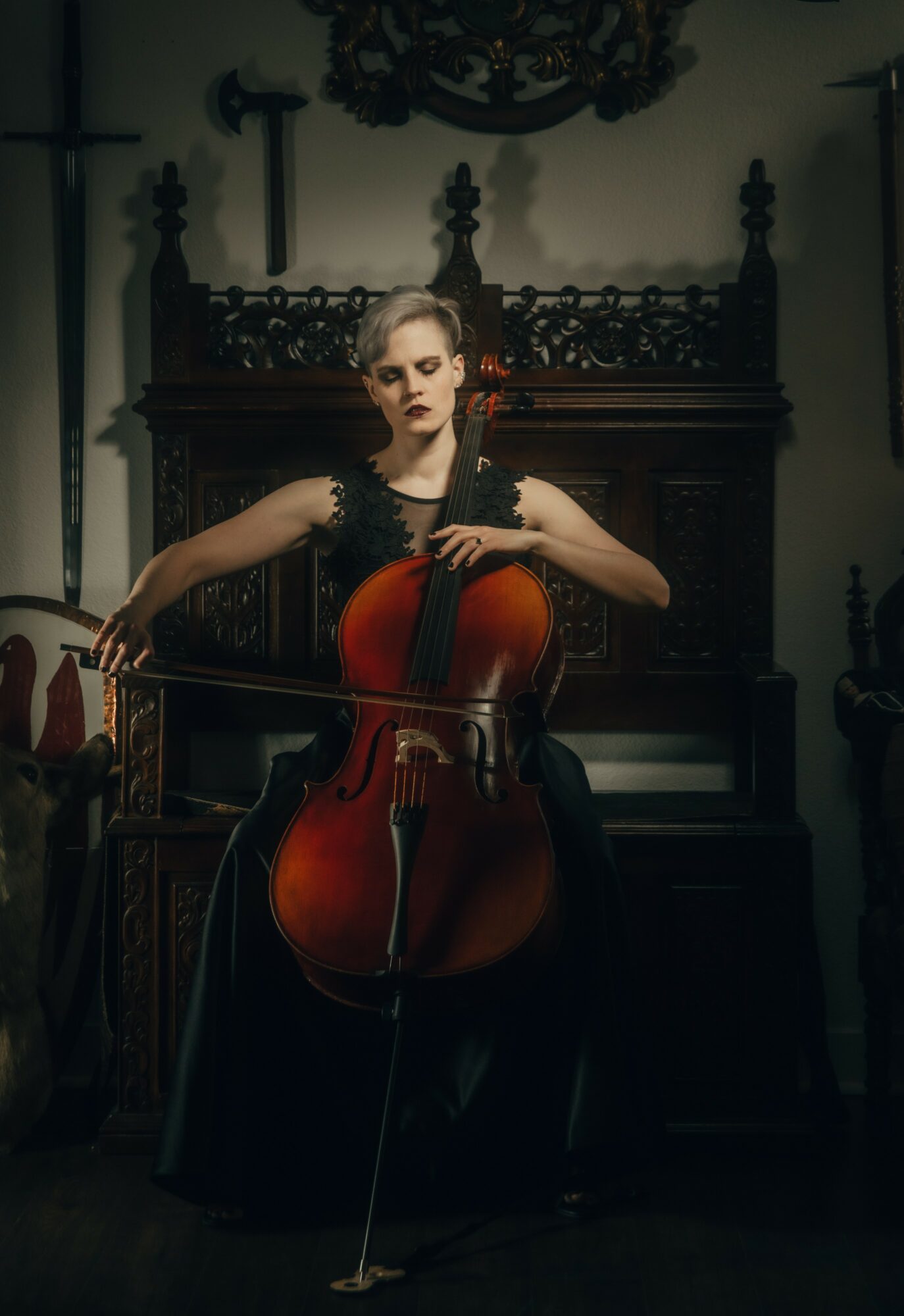 Woman playing cello in a dimly lit room with ornate wooden furniture and religious symbols on the wall.