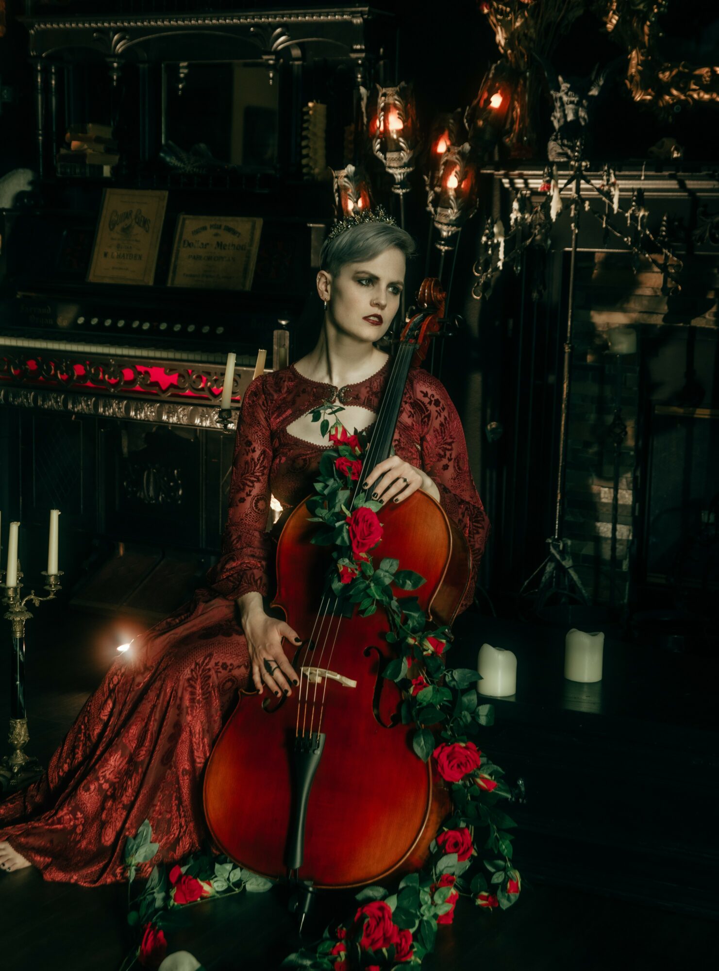 Woman in red dress holding a cello, surrounded by candles and ornate decor, in a dimly lit setting.