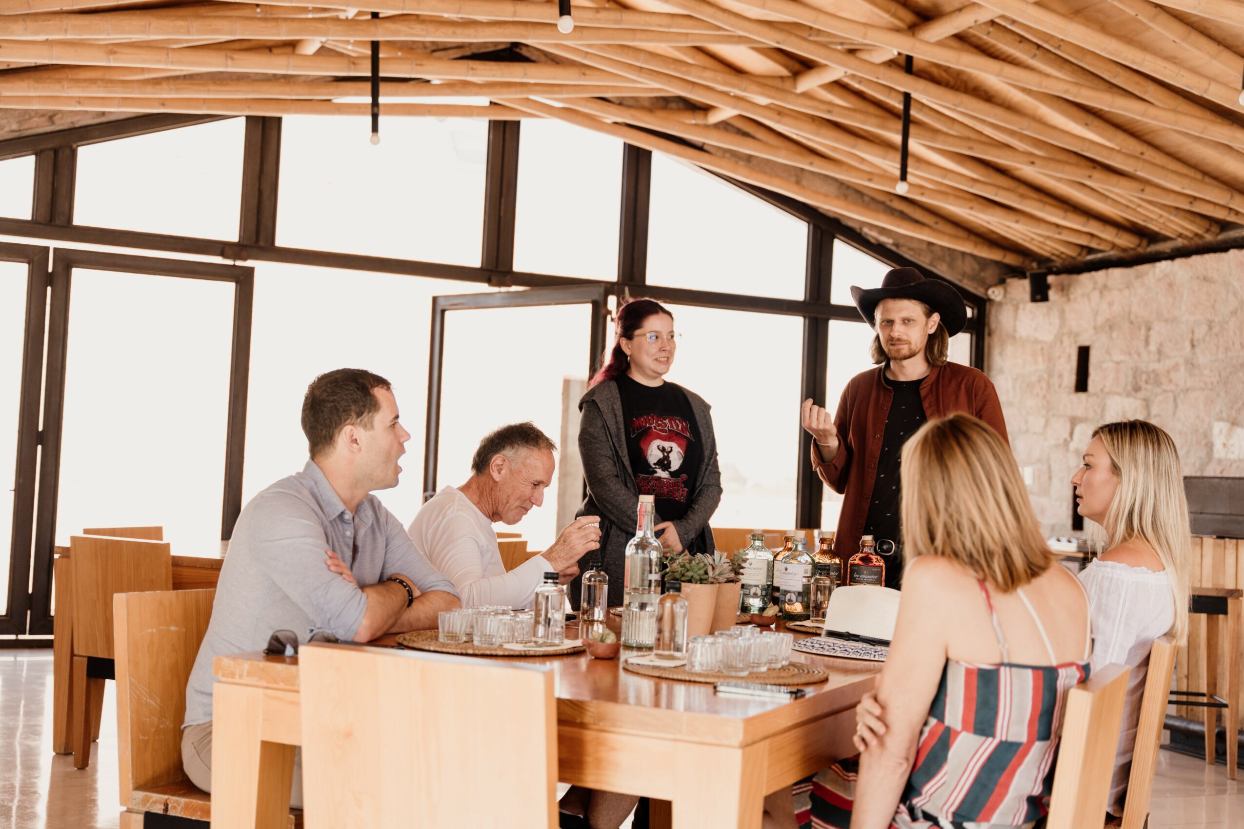 People gathered around a table in a room with large windows and a wooden ceiling, engaging in conversation.