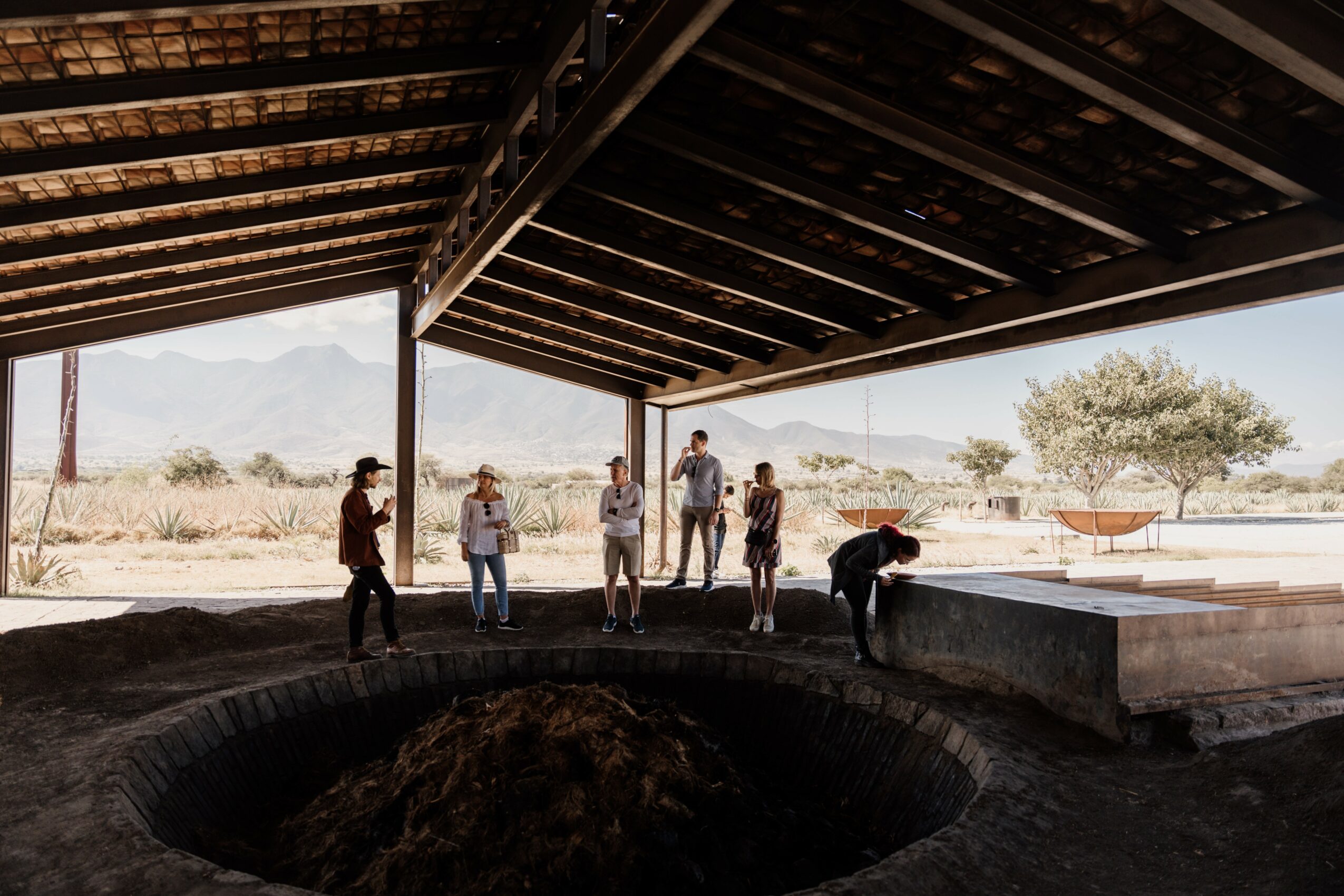 People standing under a large open structure with a view of mountains and desert landscape in the background.