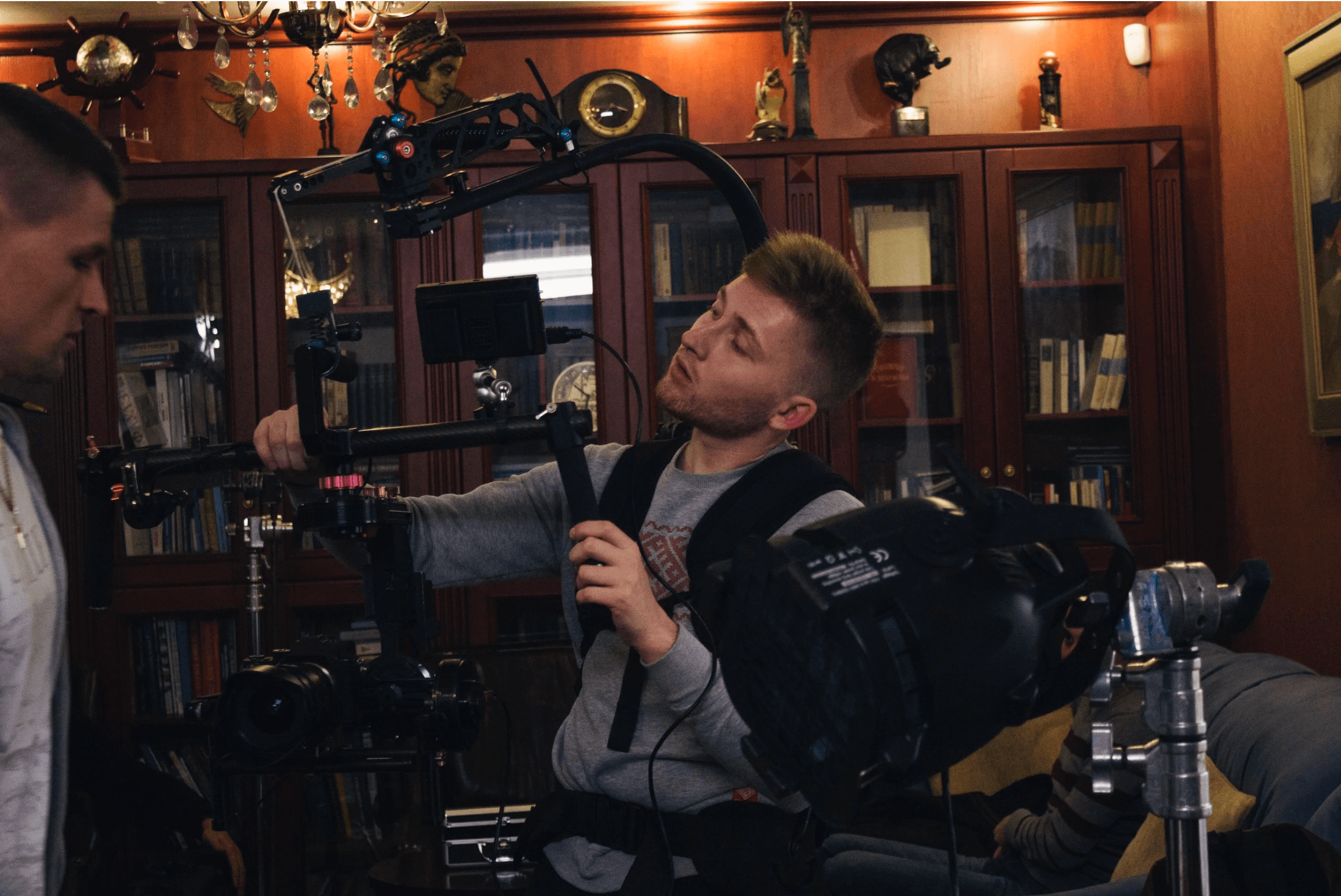 Young man operating camera equipment indoors with shelves and decorations in background.