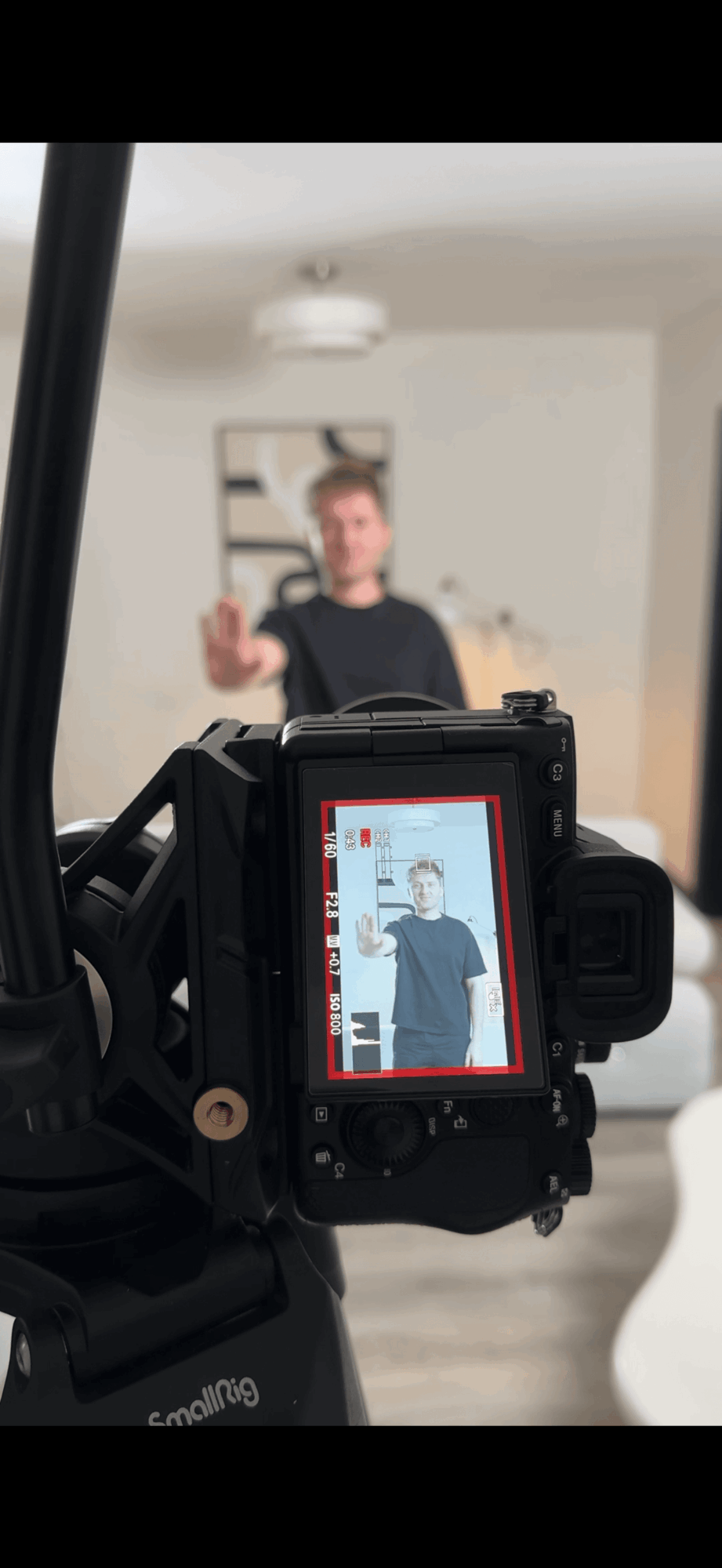 Camera view showing a person in the background taking a selfie, with the camera screen displaying the person. Word count: 20