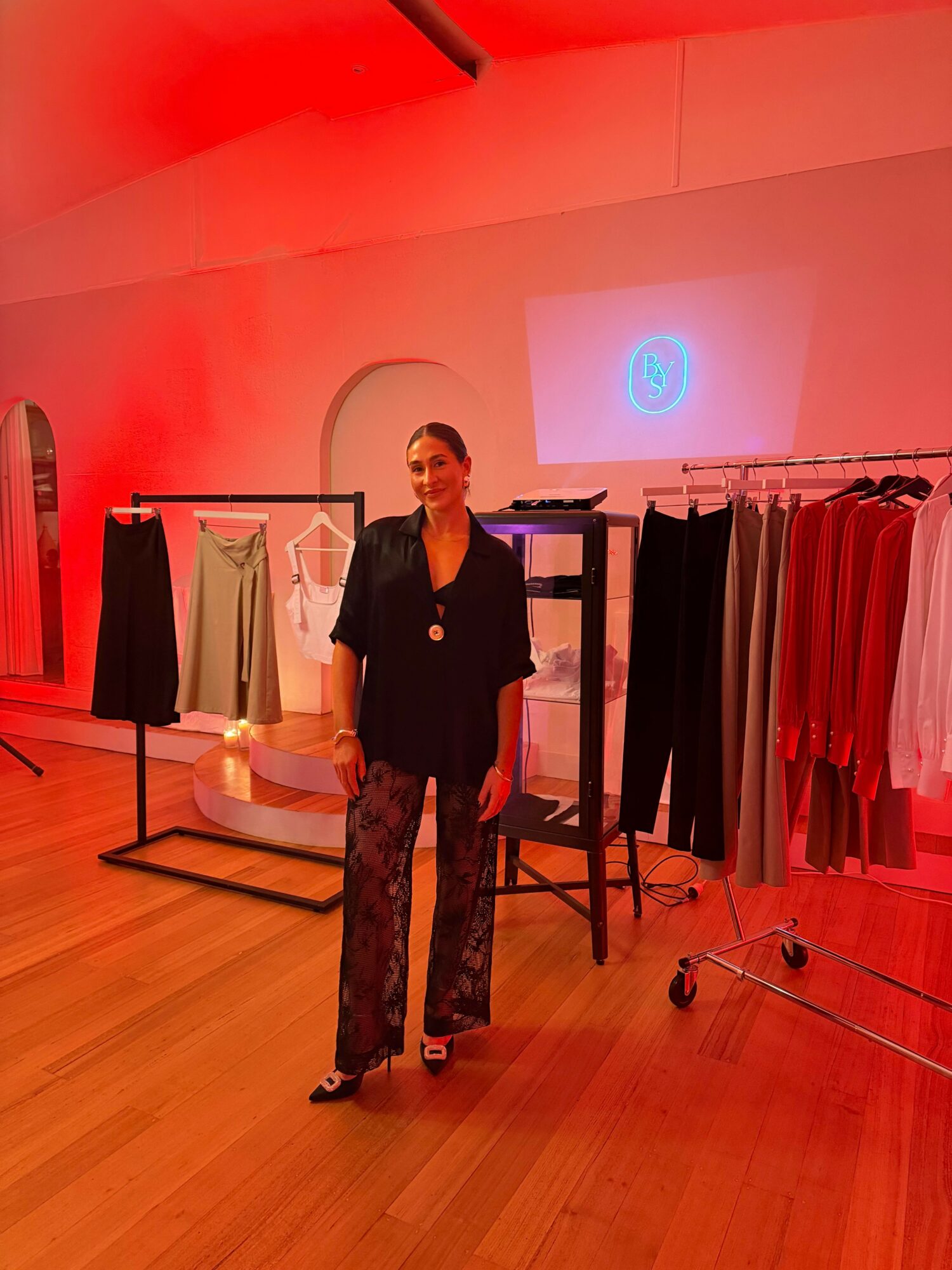 Person standing in a room with clothing racks, illuminated by red lighting, with a projection on the wall.