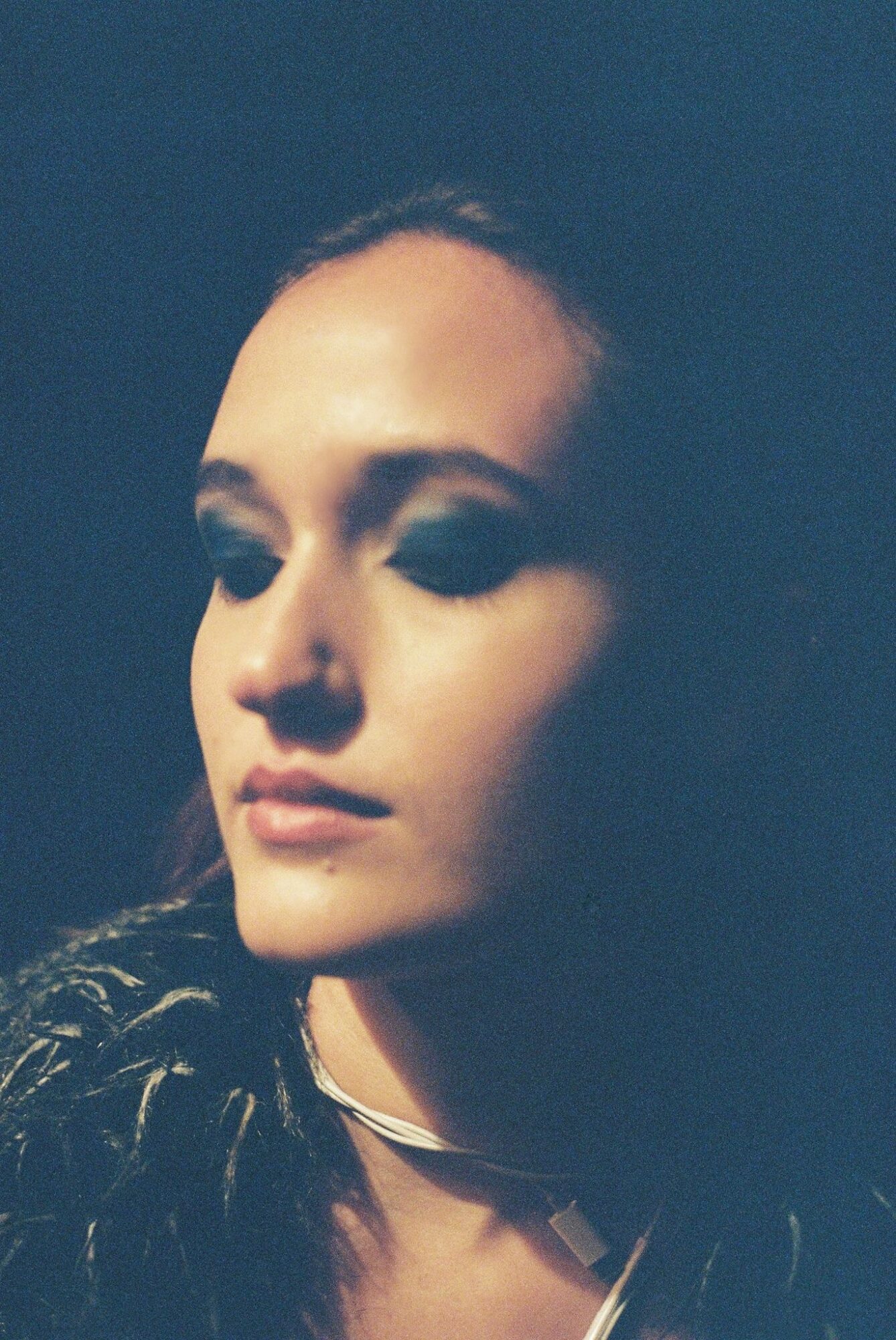 Portrait of a woman with closed eyes and dark hair, illuminated face, dark background.