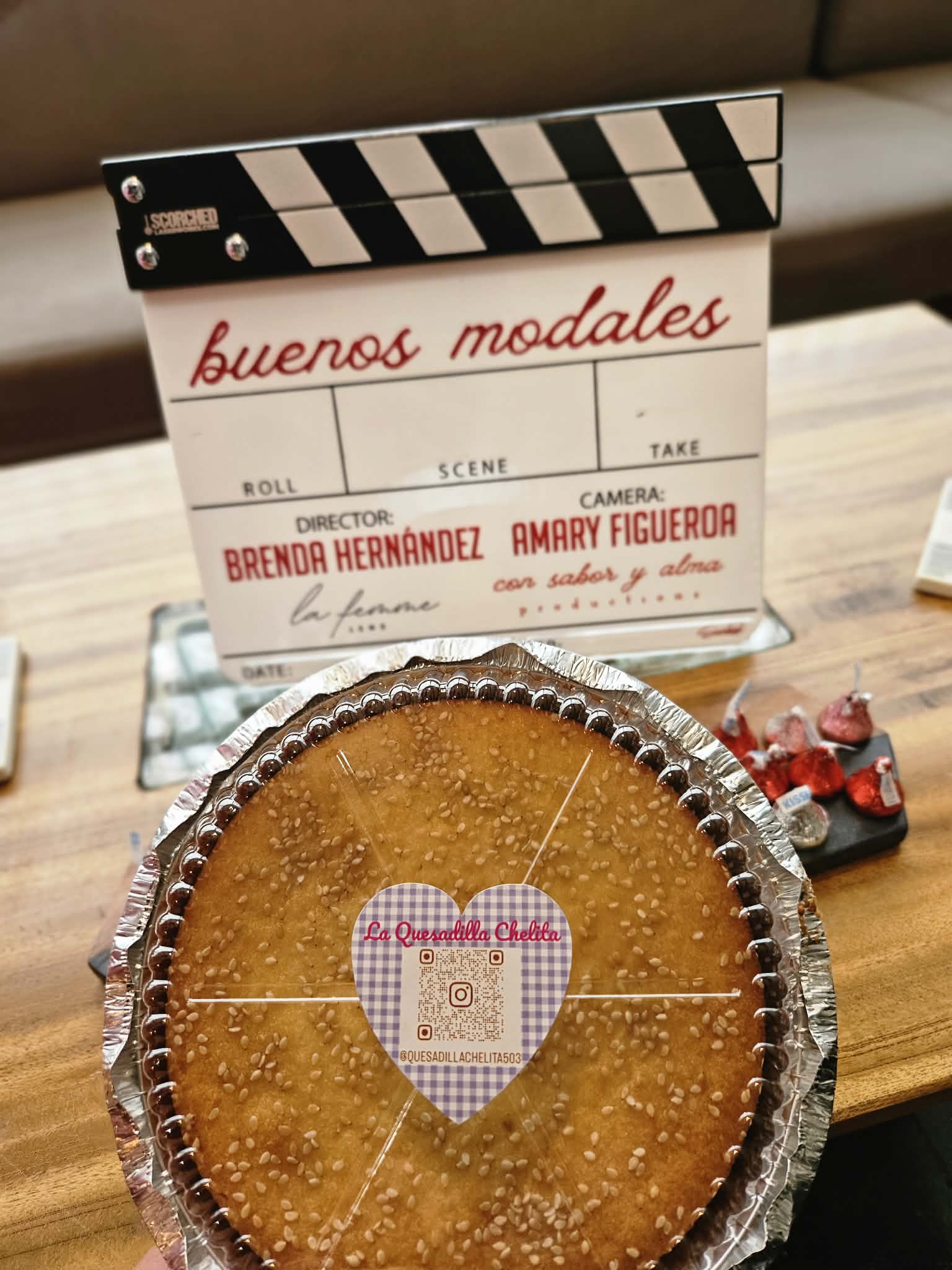 Round cake with a heart-shaped decoration in the center, placed on a wooden table with a film clapperboard in the background.