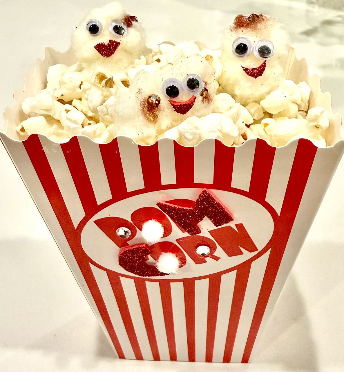 Popcorn container with three popcorn pieces decorated with googly eyes and smiles, labeled 'Popcorn' in red and white stripes.