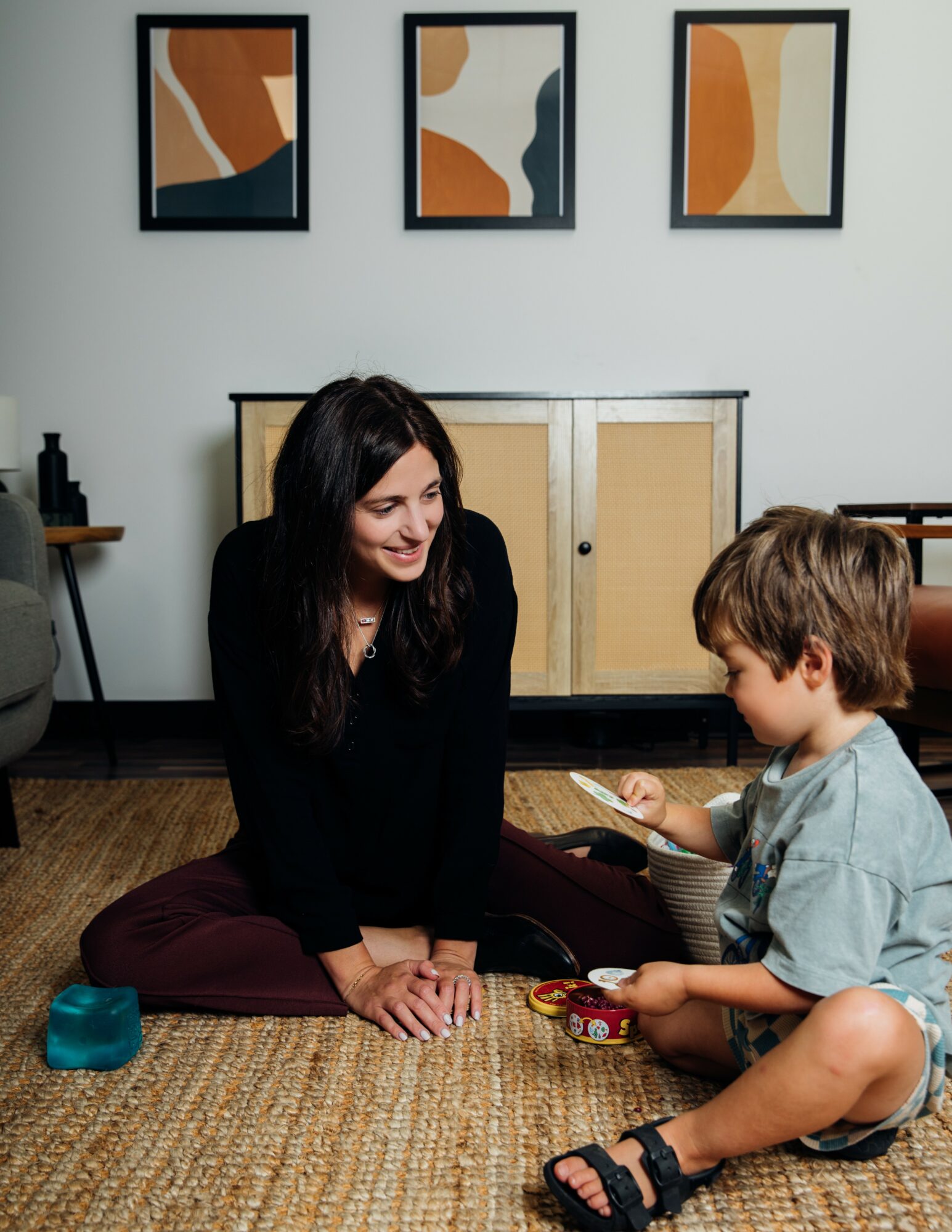 Woman and child sitting on a rug, playing a game together in a room with abstract art on the wall.