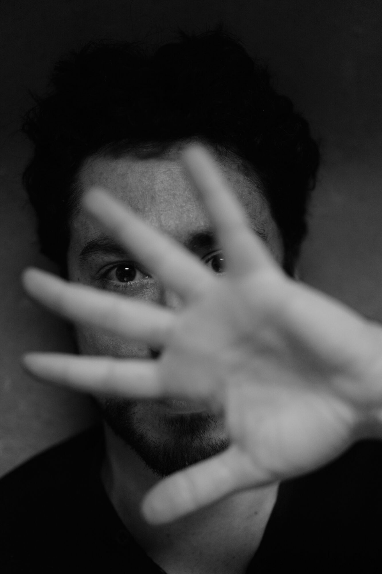 Person with dark curly hair partially covering face with hand, eyes visible, black and white photo.